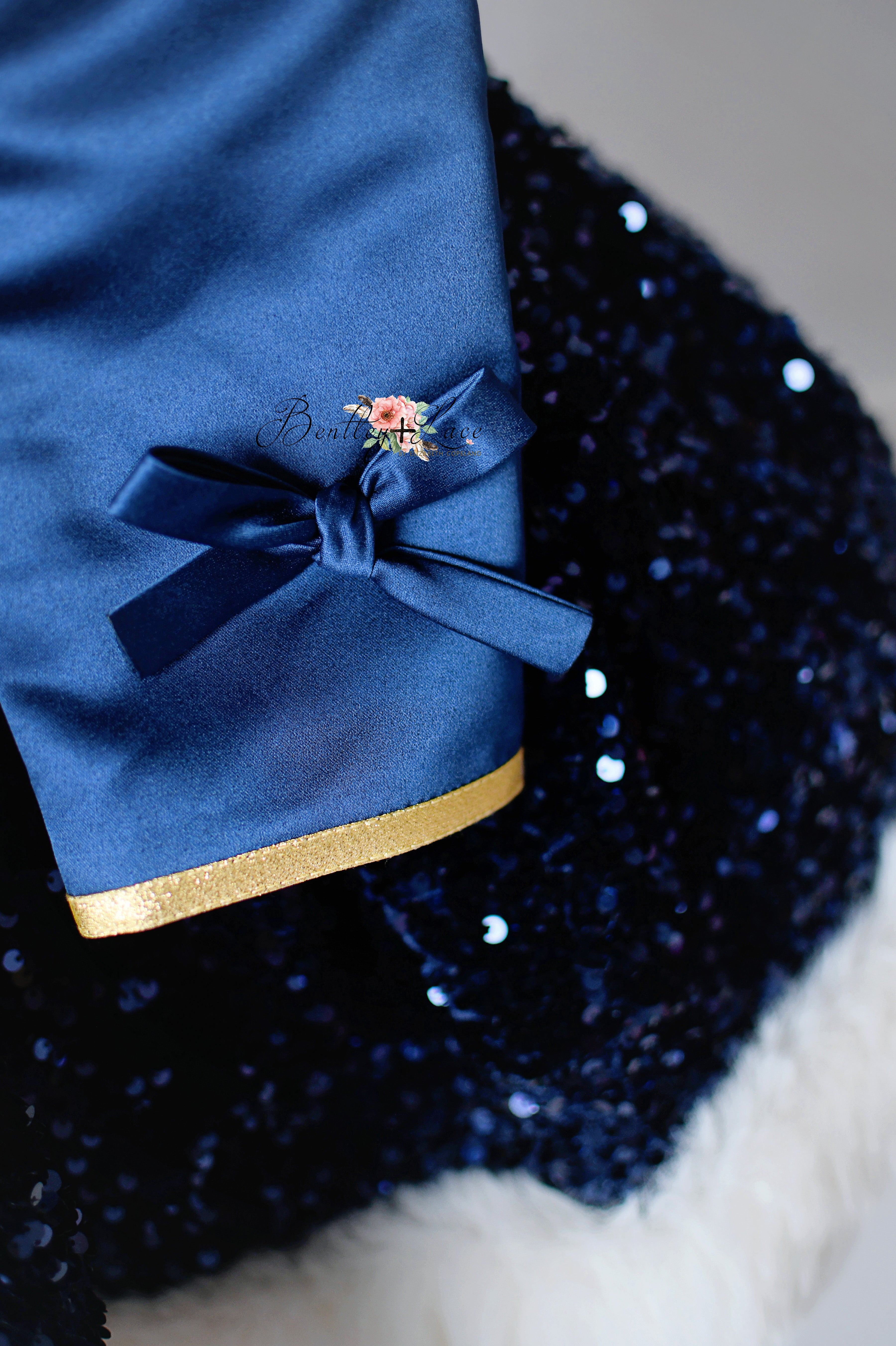 Close-up of a blue fabric with a bow and gold trim on a dark sequined background.