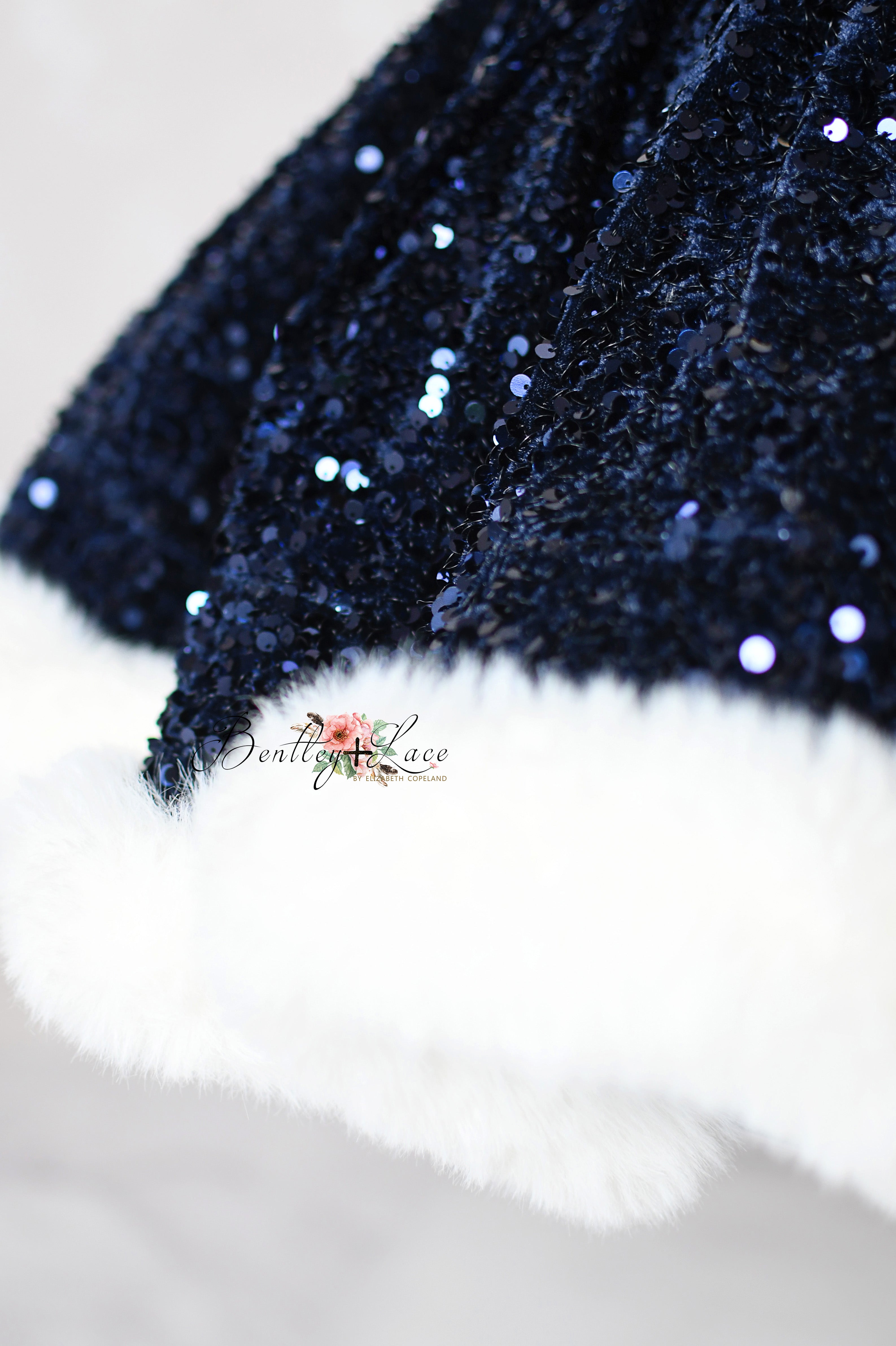 Close-up of a dark blue sequined fabric with white fur trim on a light background.