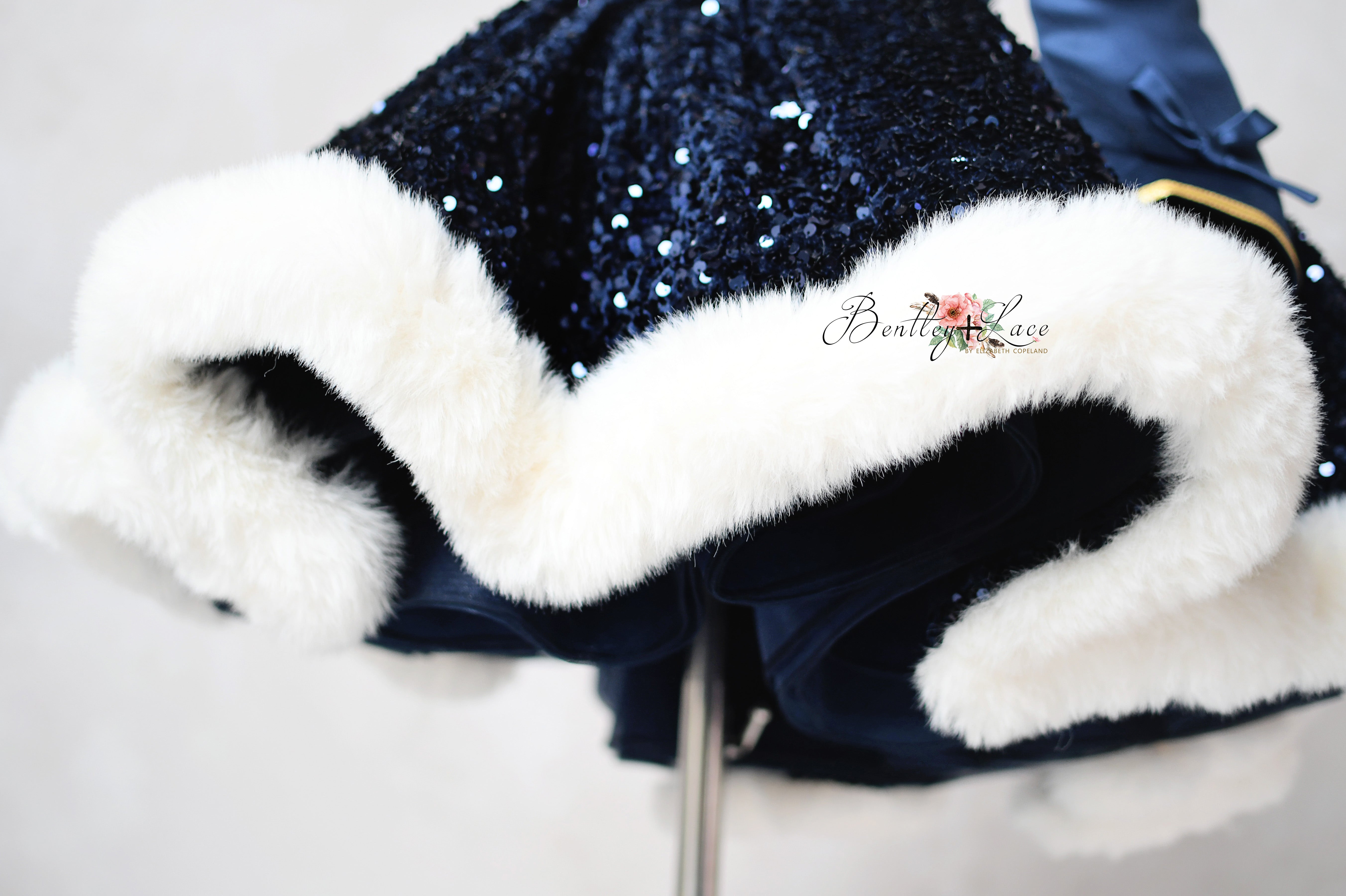 Navy blue sequin dress with white fur trim on a light gray background