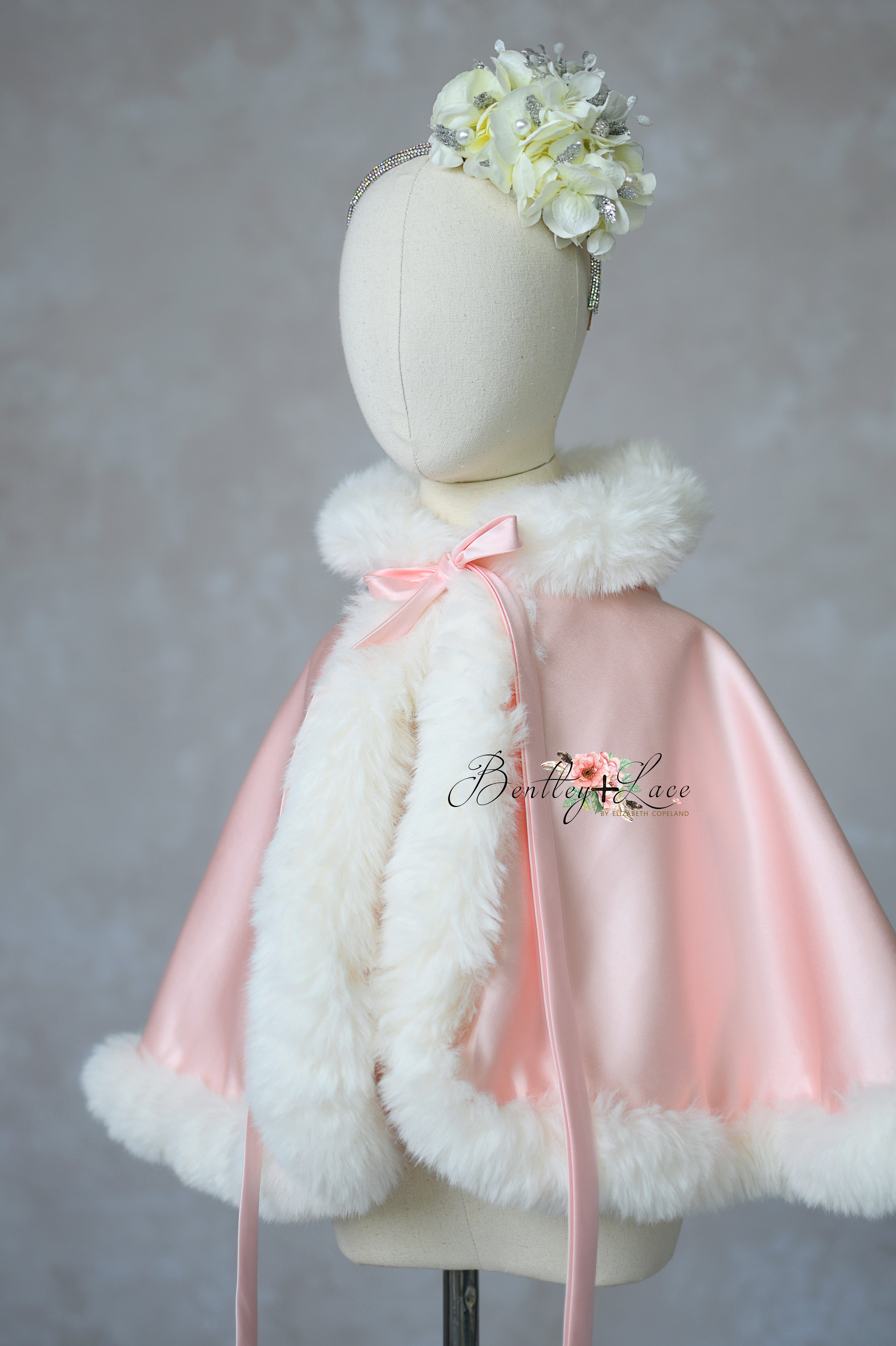 Pink cape with white fur trim on a mannequin against a plain background