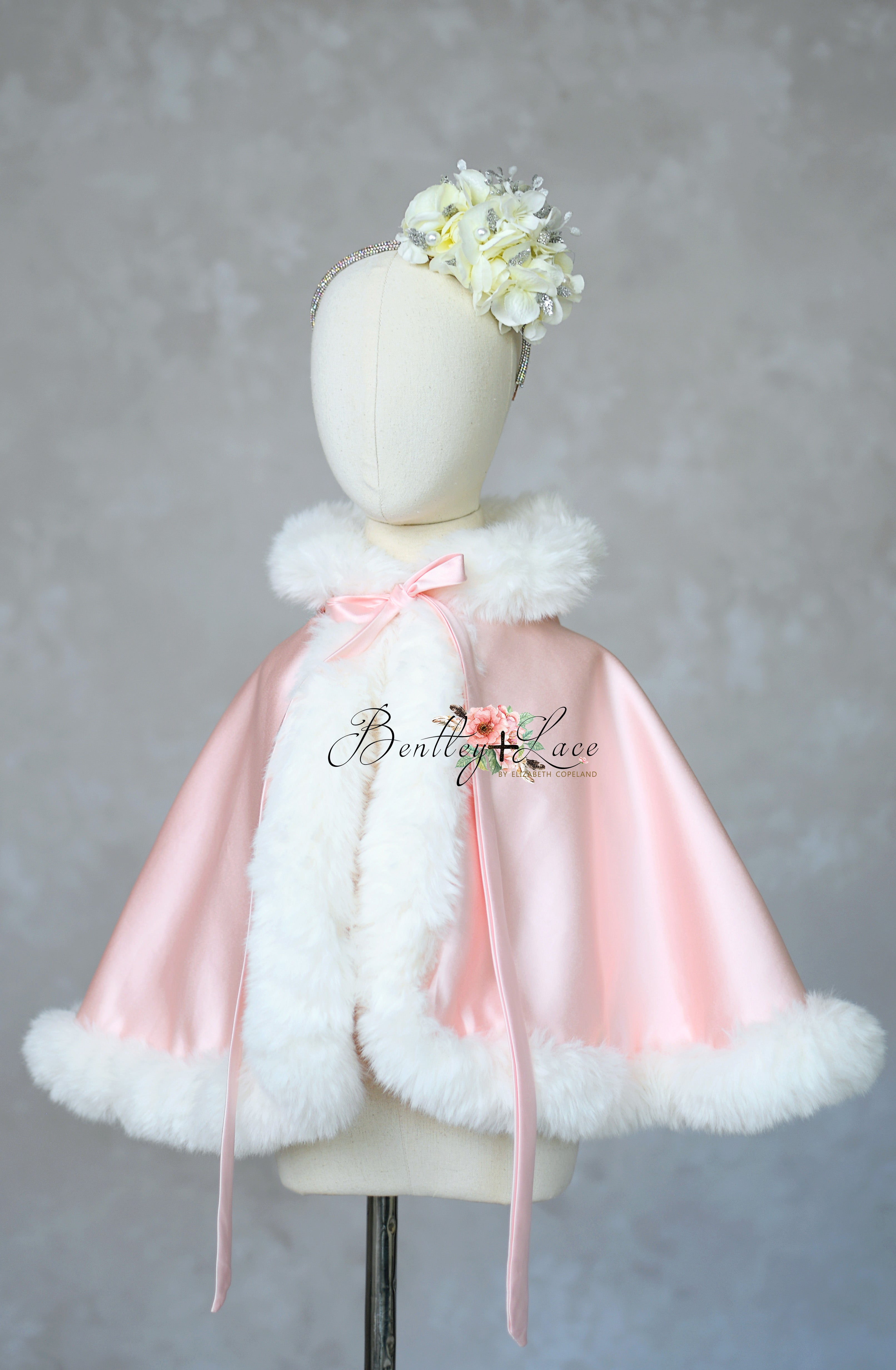 Pink cape with white fur trim on a mannequin against a gray background