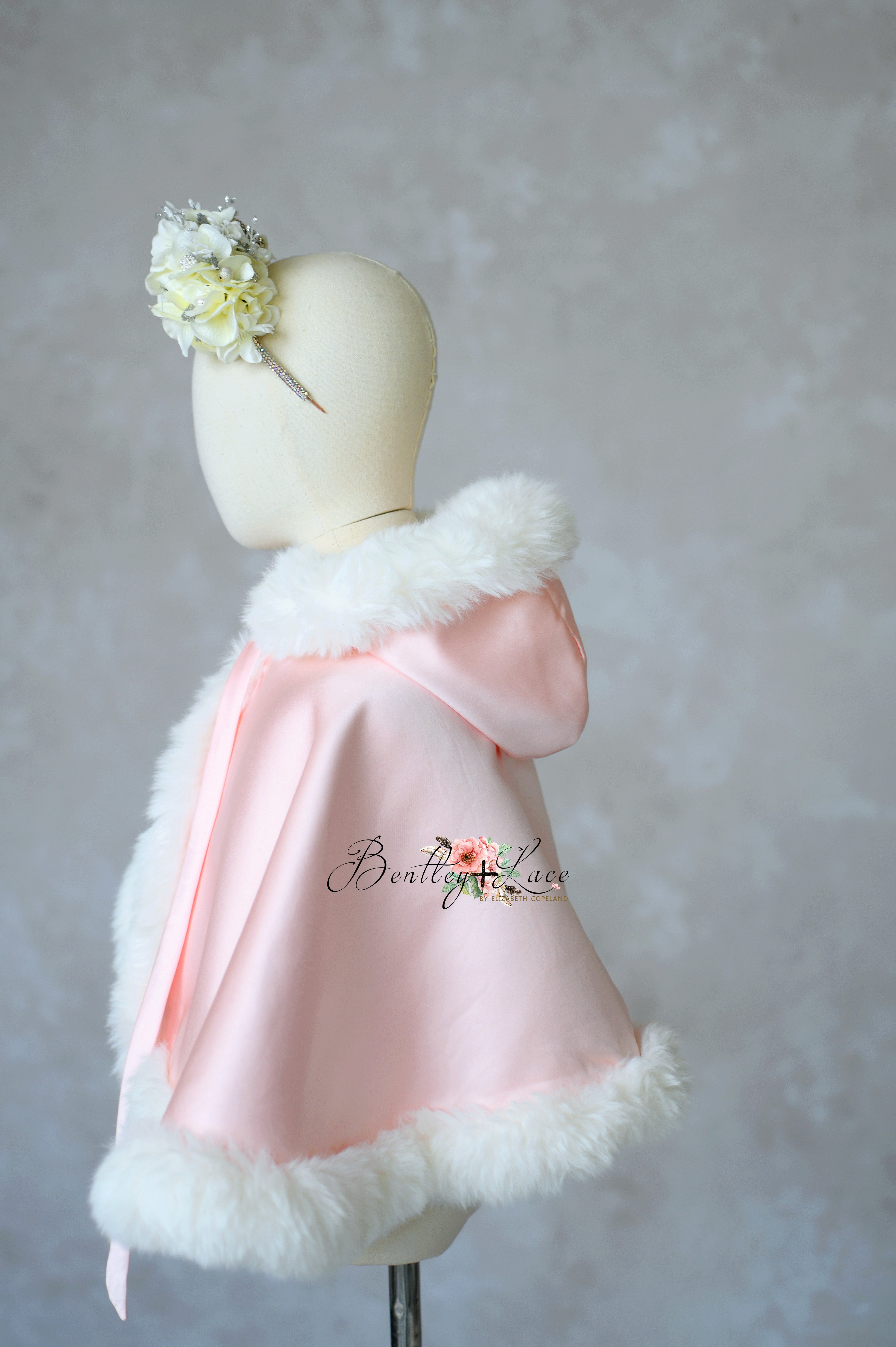 Pink satin cape with white fur trim on a mannequin against a plain background