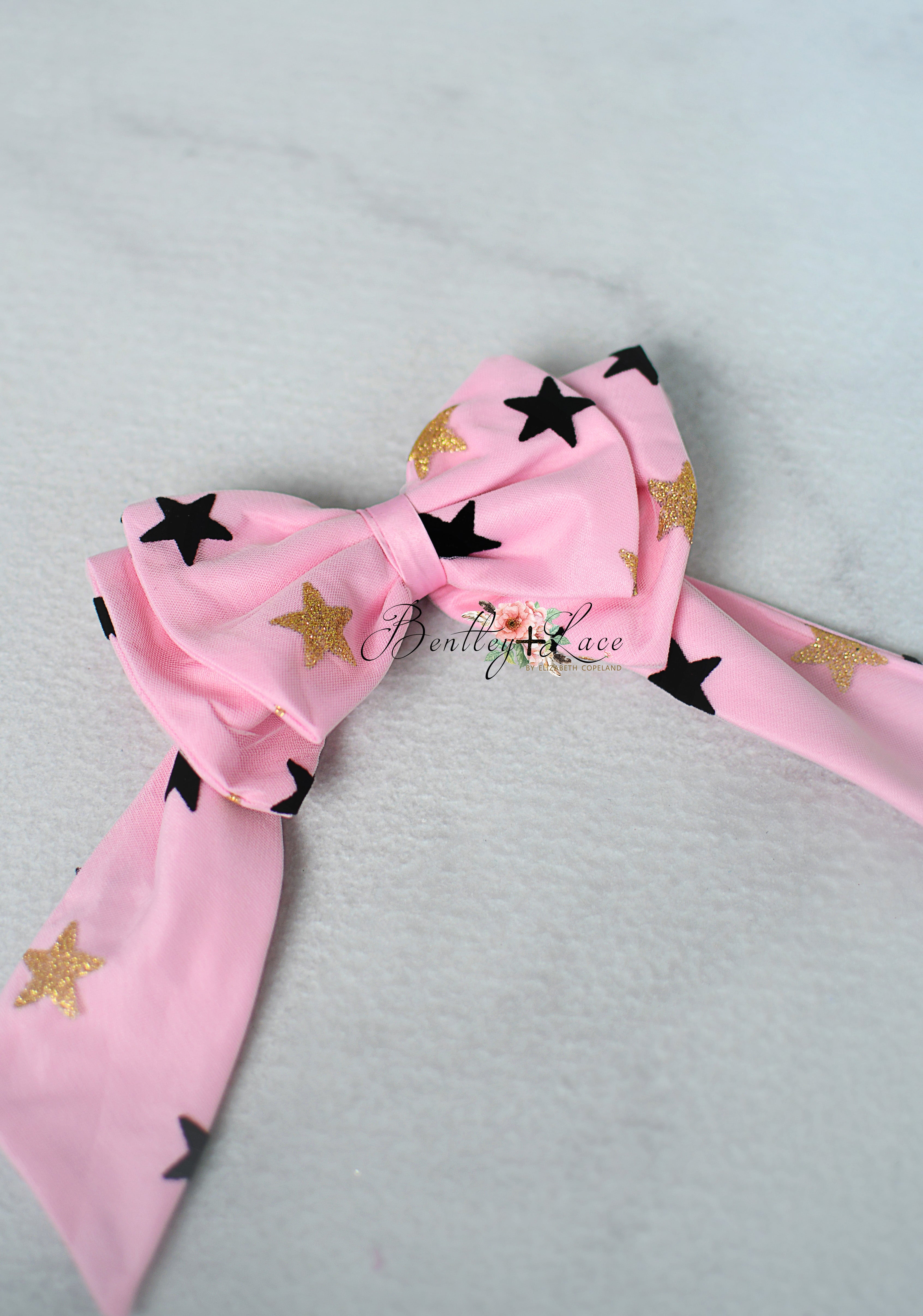 Pink bow with black and gold star patterns on a light gray background