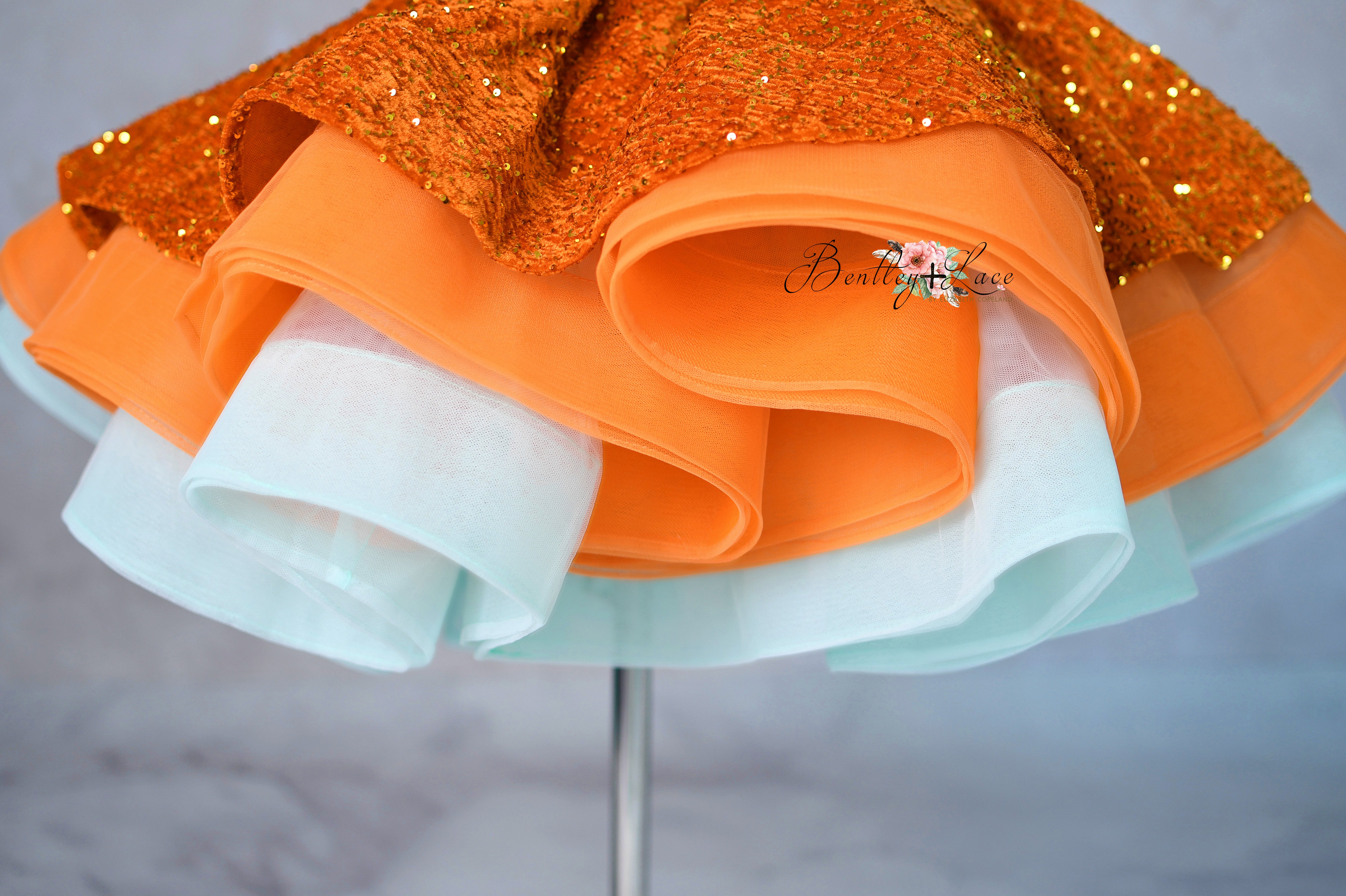 Large orange bow with glittery top on a stand against a neutral background
