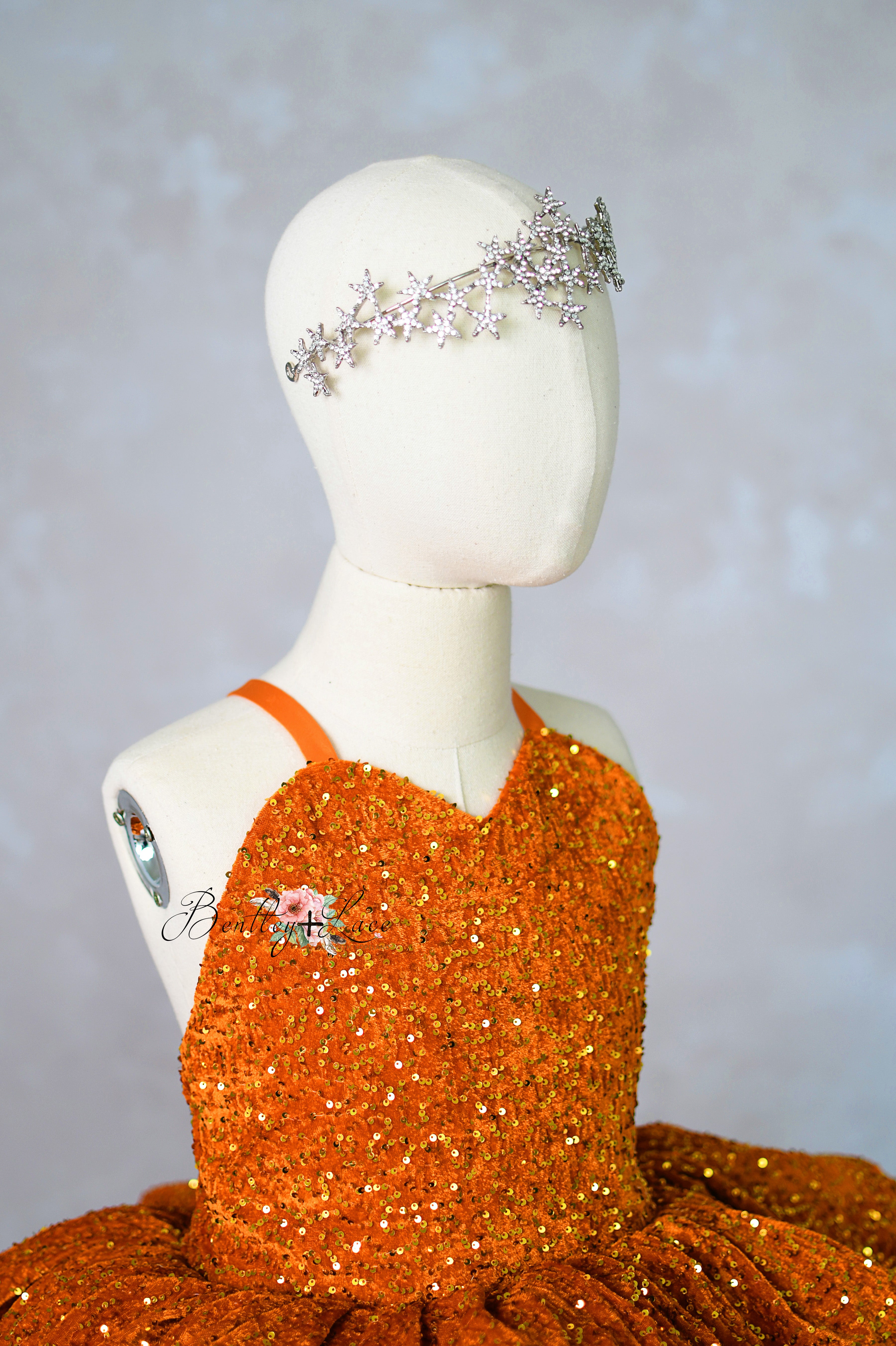 Mannequin wearing an orange sequined dress with a silver headpiece against a gray background