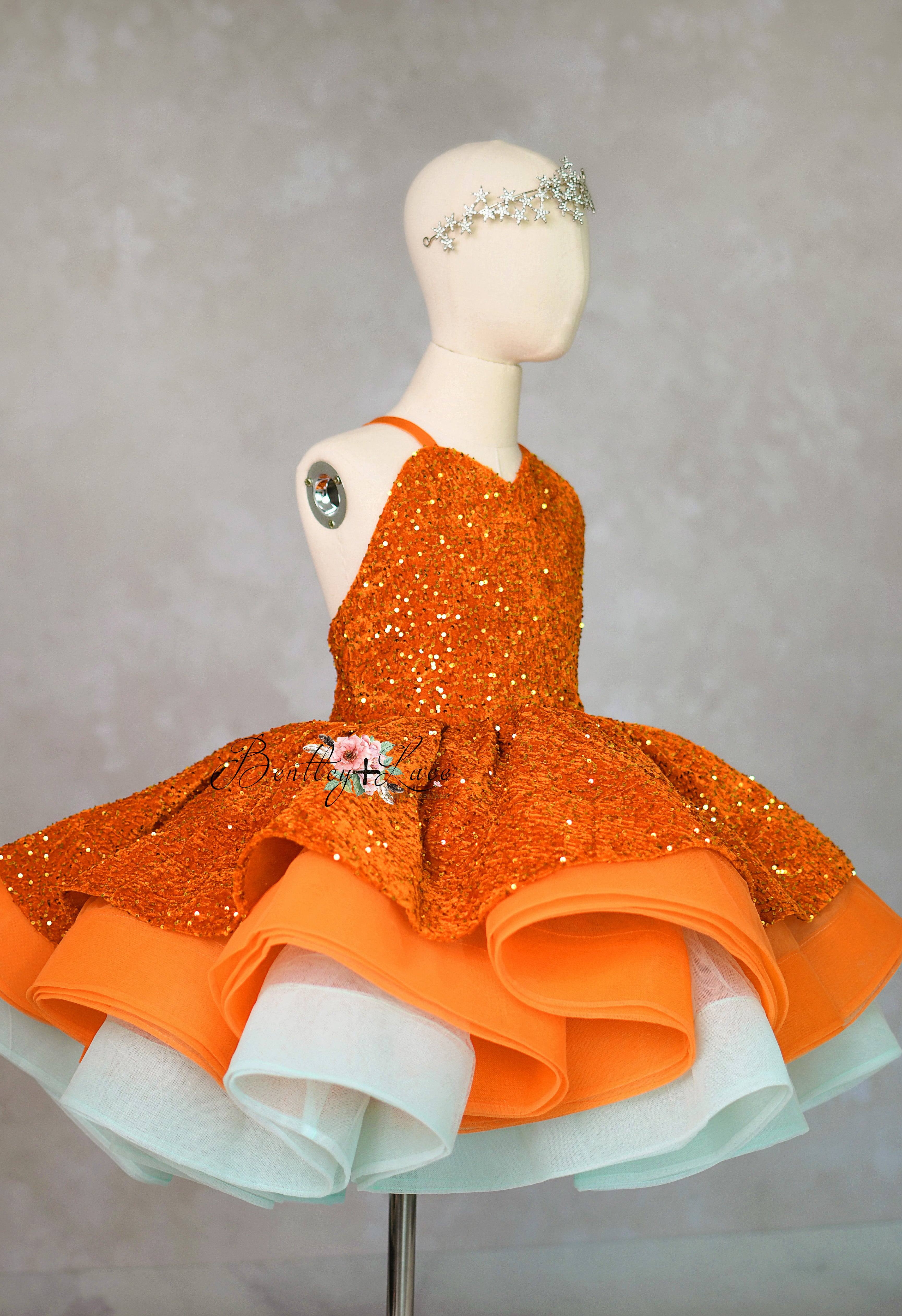 Orange sequined dress with a white skirt on a mannequin against a gray background
