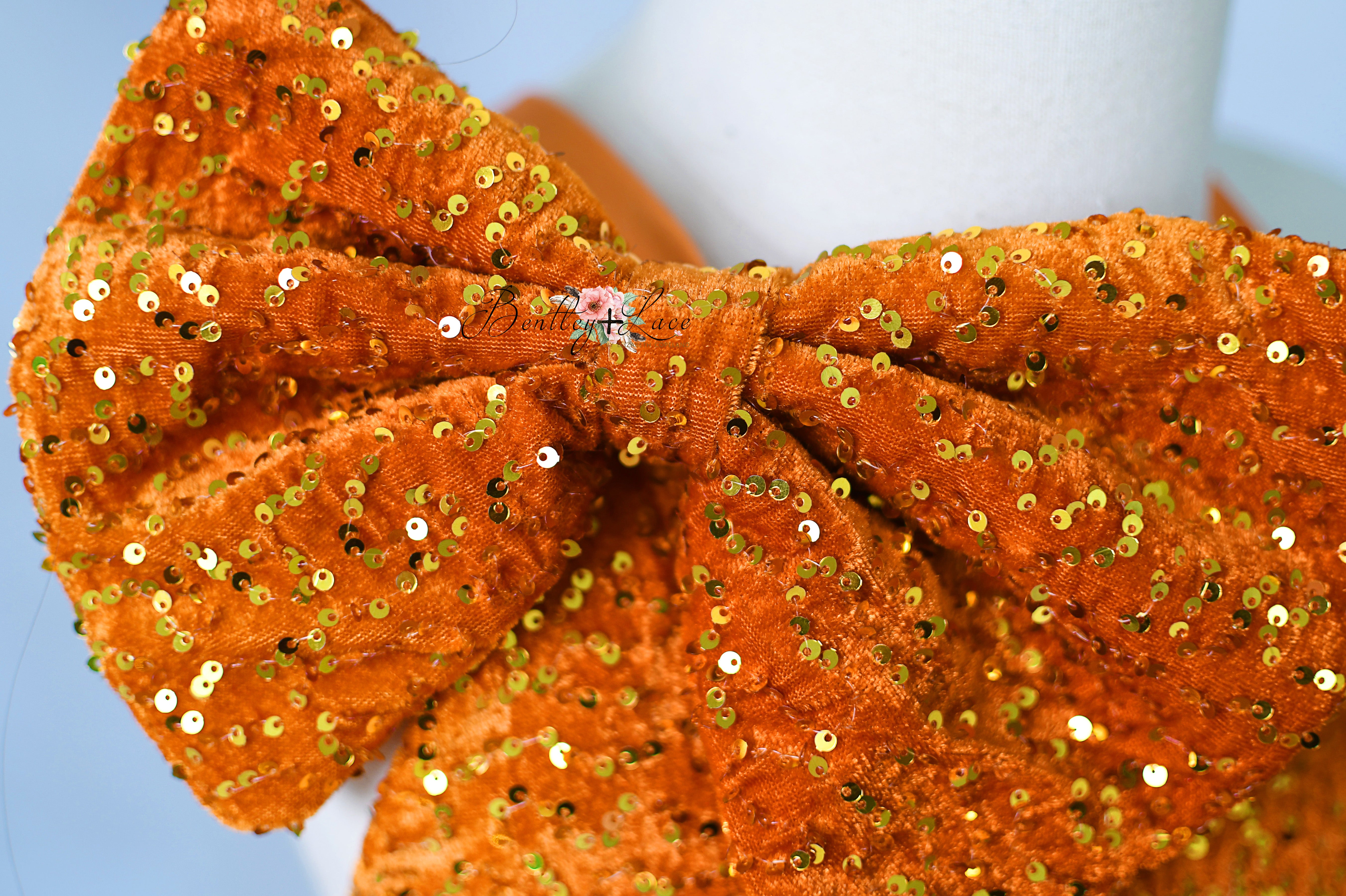 Orange sequin bow headband on a light blue background