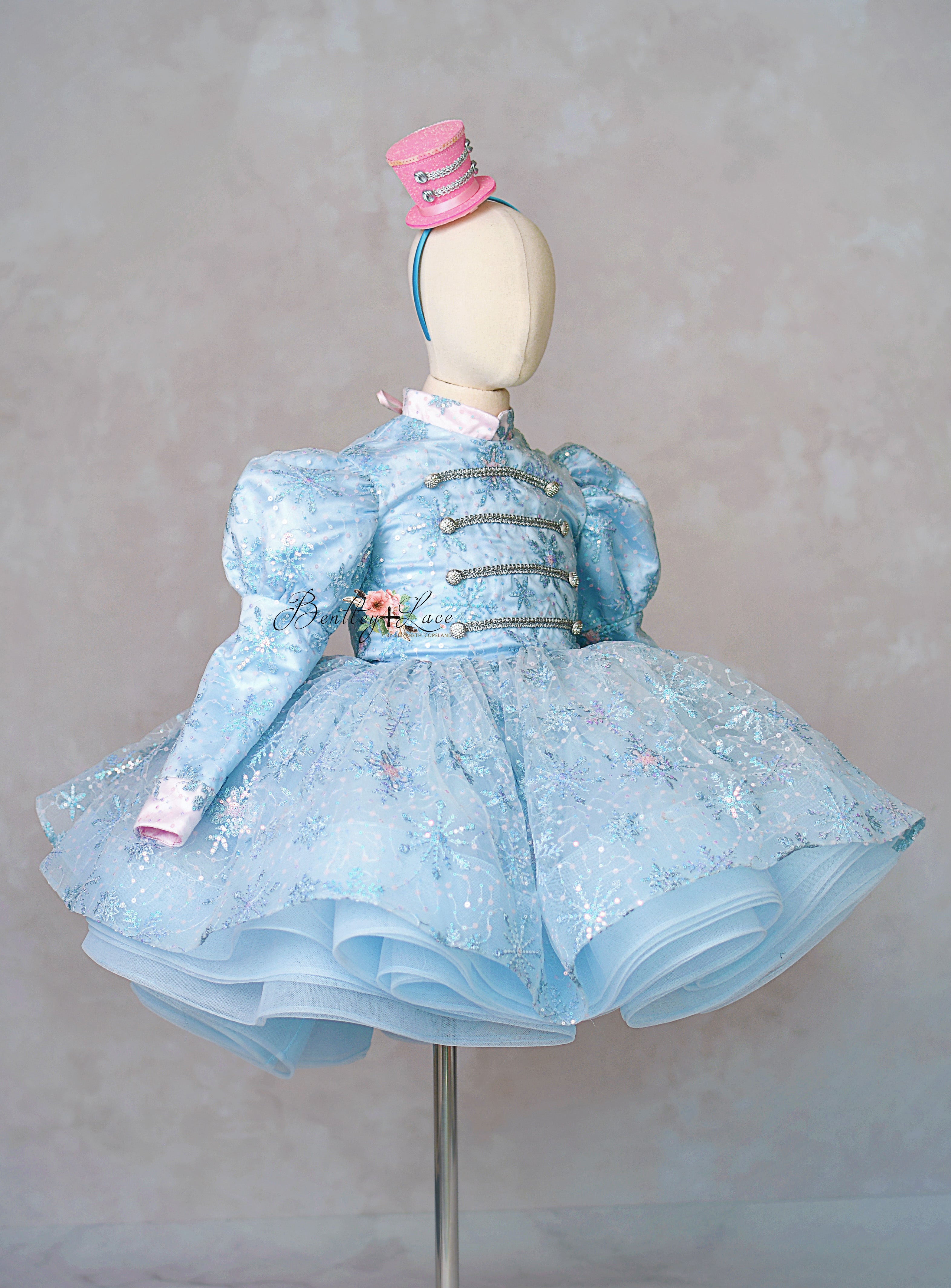 Mannequin wearing a light blue dress with ruffles and a pink hat on a gray background