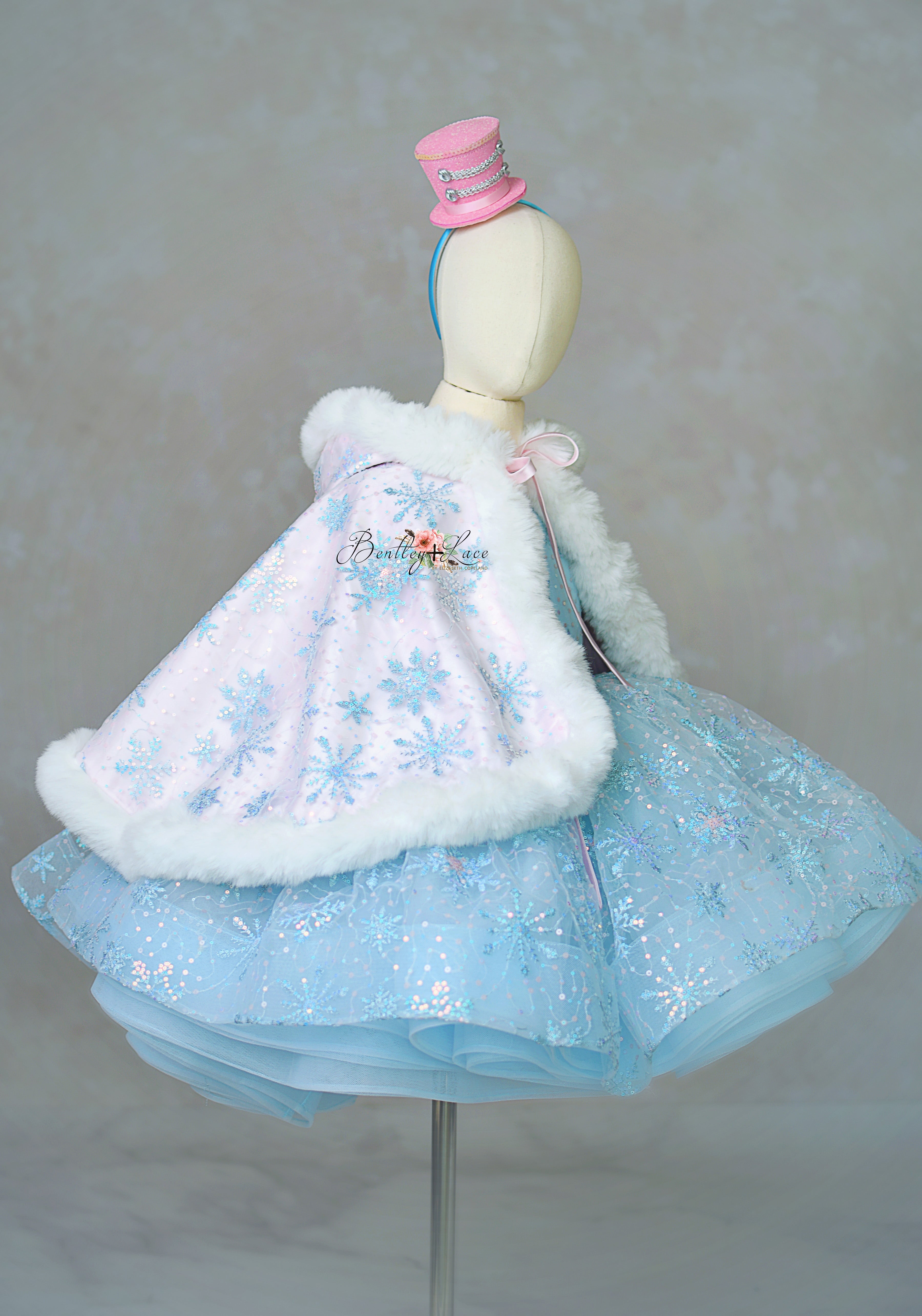 Mannequin wearing a light blue dress with snowflake patterns and white fur trim on a neutral background.