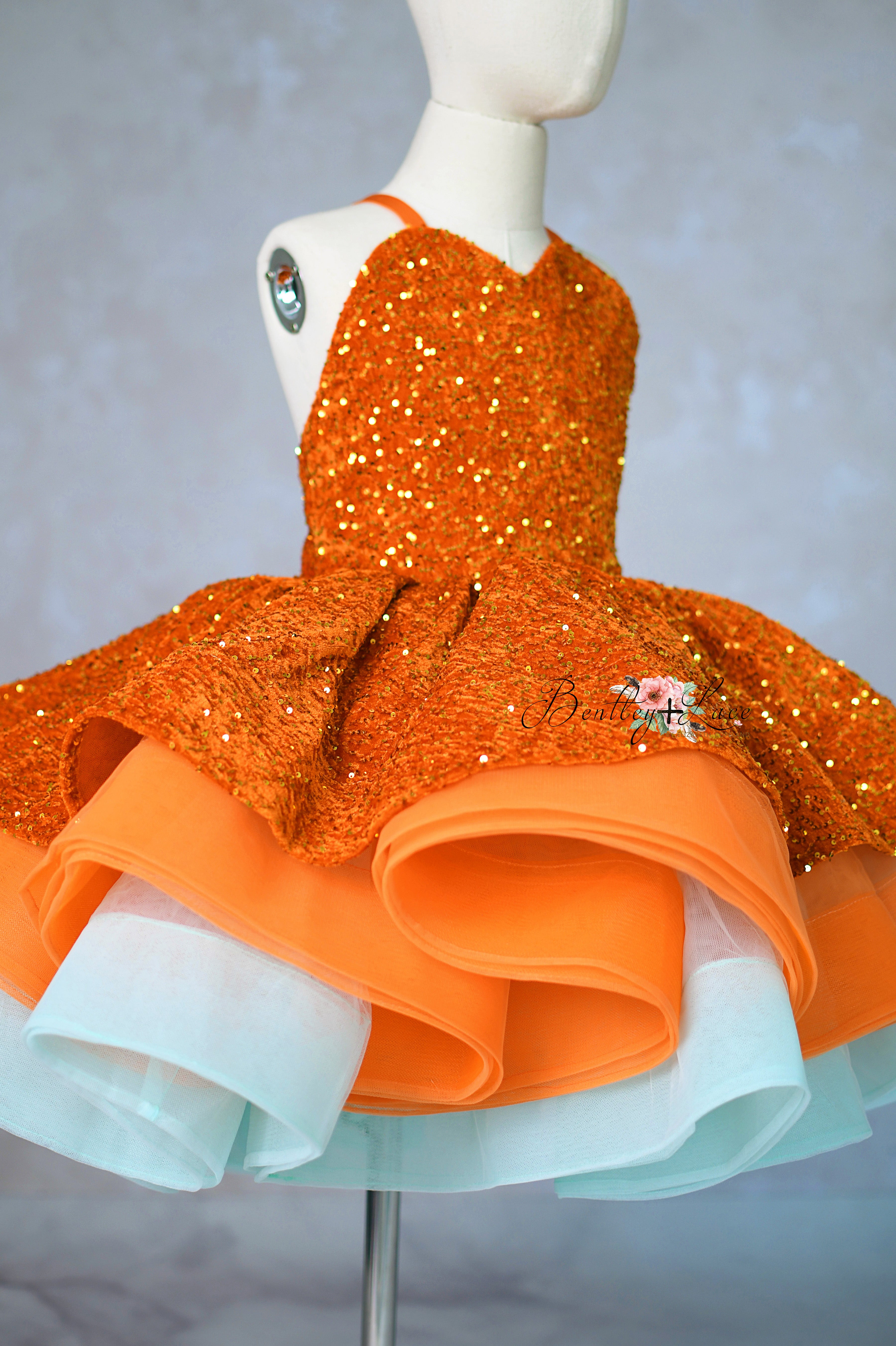 Orange sequined dress on a mannequin against a gray background