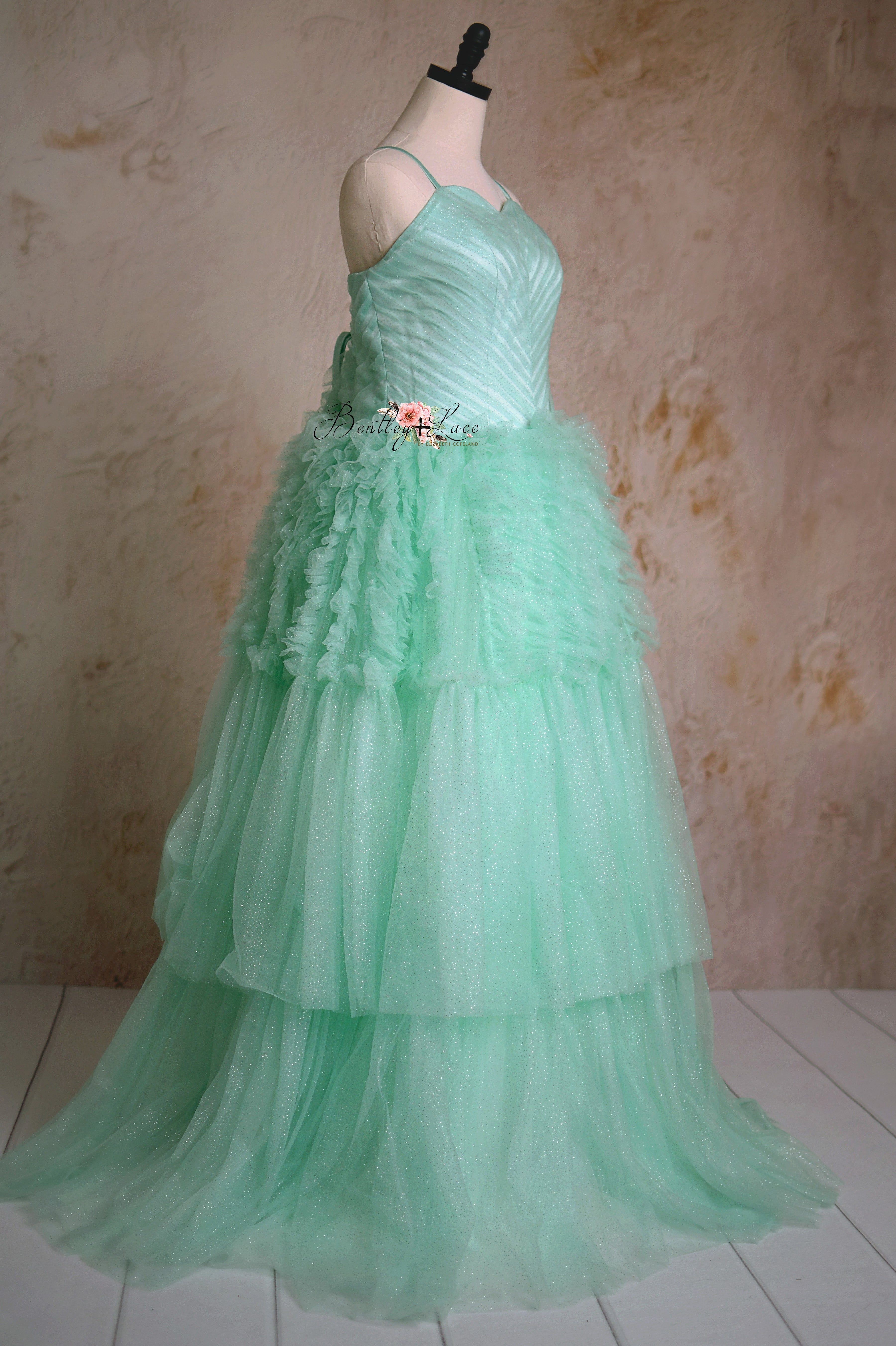 A mother and daughter twirl in matching pastel couture gowns in front of a painterly lavender-toned background.
