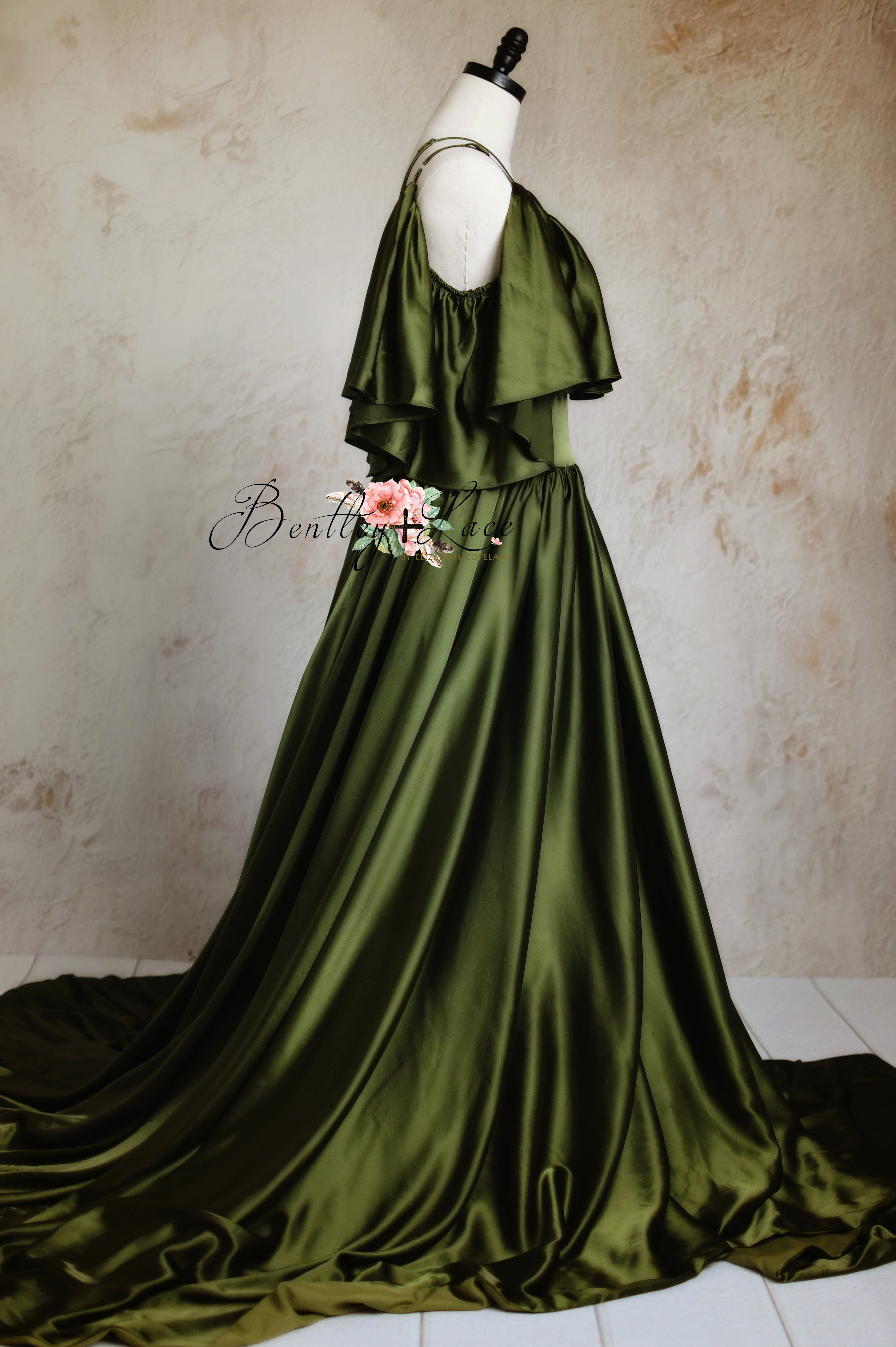 Dramatic green dress with a floor-sweeping train, displayed against a dreamy pink and gray backdrop.