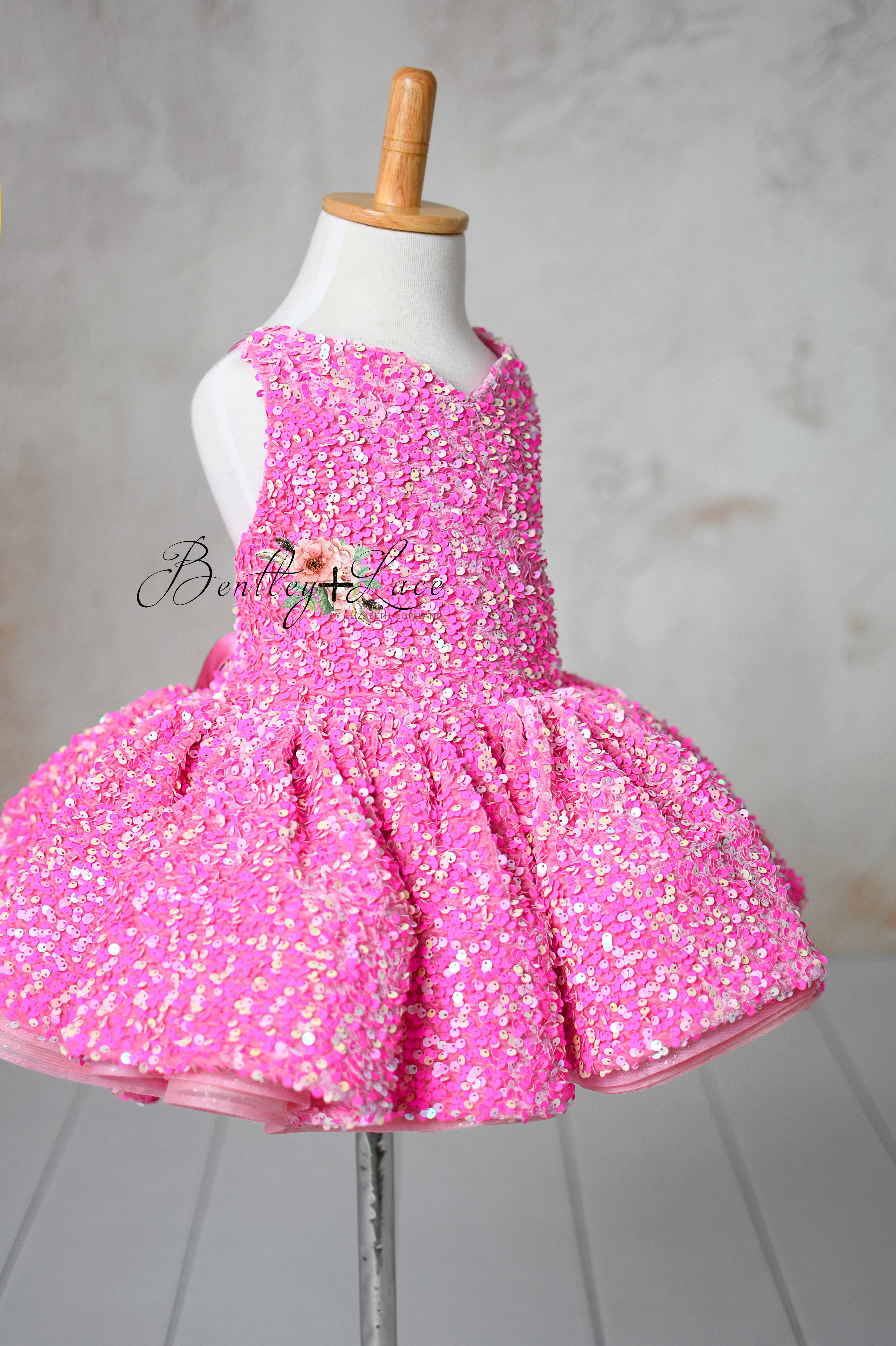A bright pink sequin dress for toddlers displayed on a mannequin, featuring a fitted bodice and voluminous skirt, with intricate shimmering details.