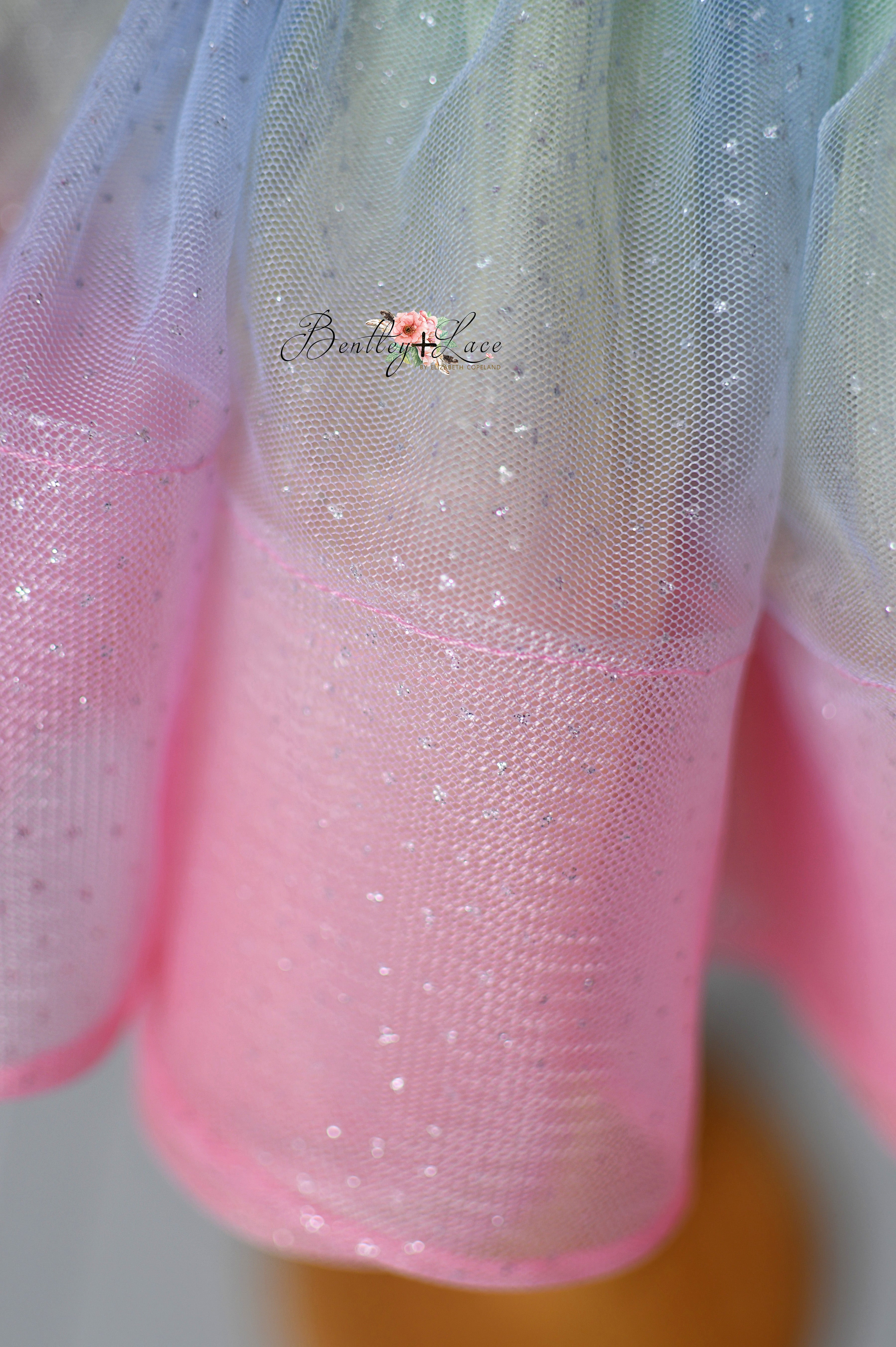 A sparkly children's gown adorned with hot pink and iridescent sequins, styled with a sleeveless design and layered skirting.