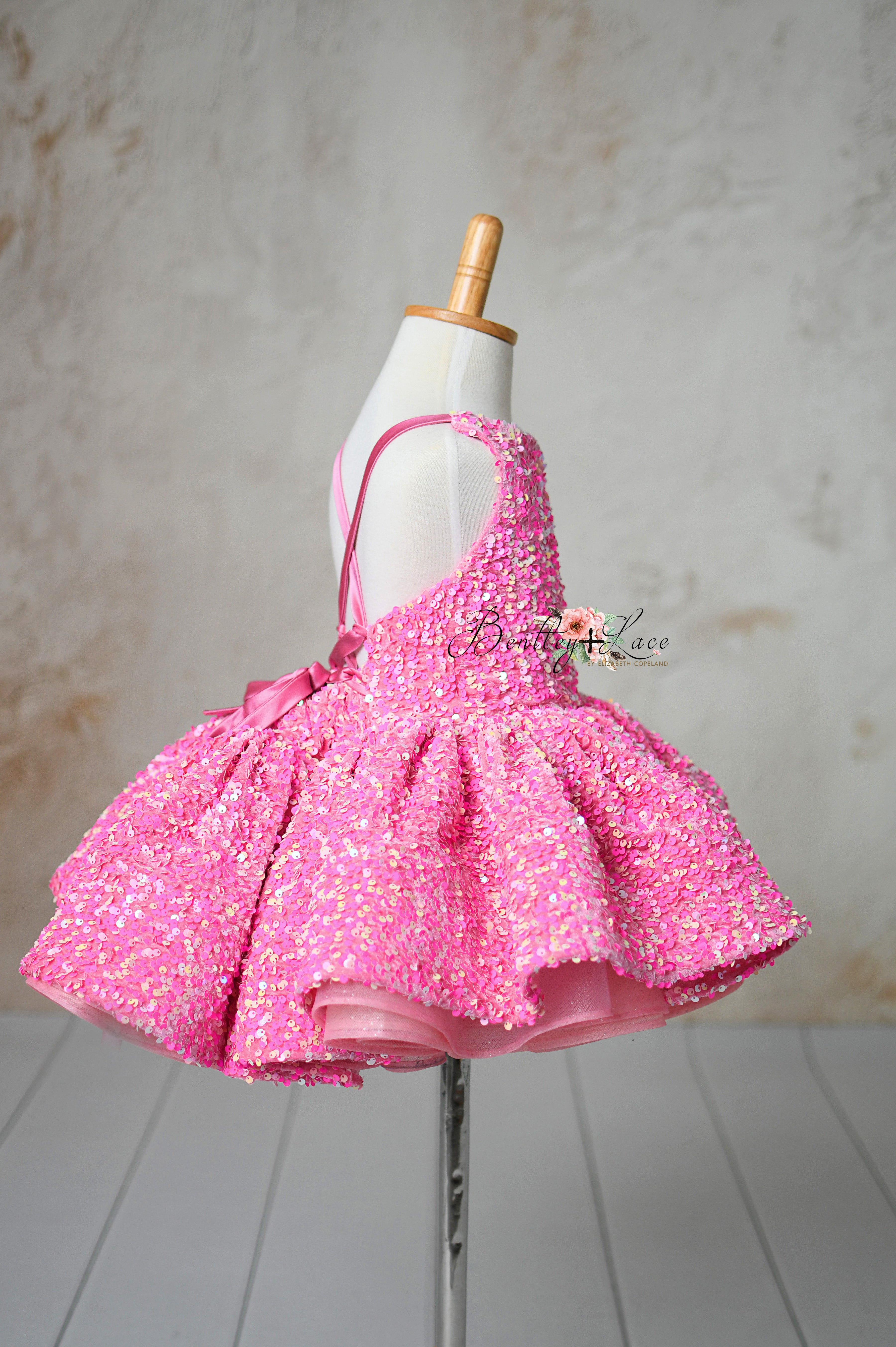 A dazzling pink dress covered in sequins, perfect for special occasions, shown on a mannequin against a neutral background.