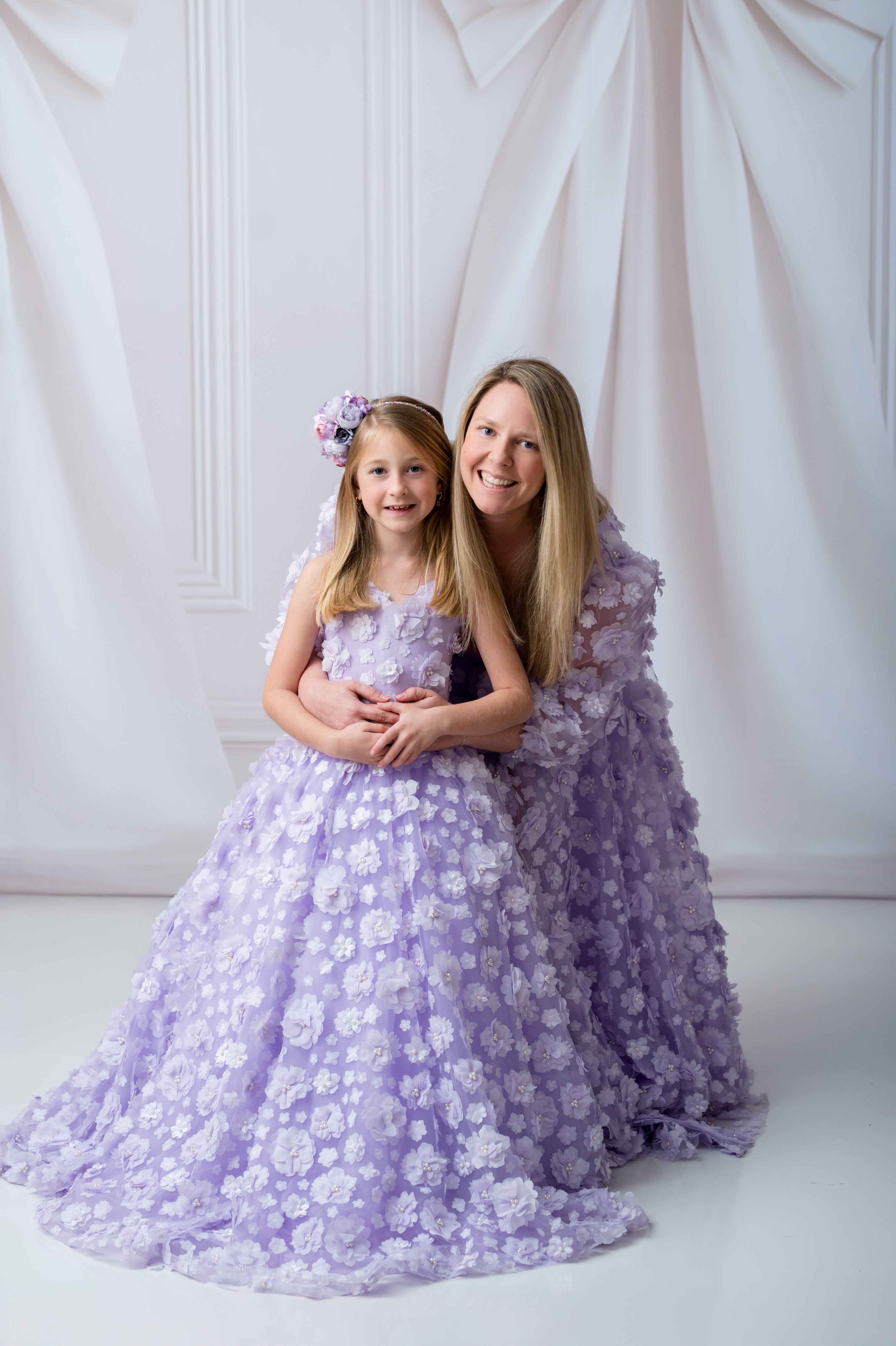 Woman and young girl in matching lavender floral dresses posing against a white background