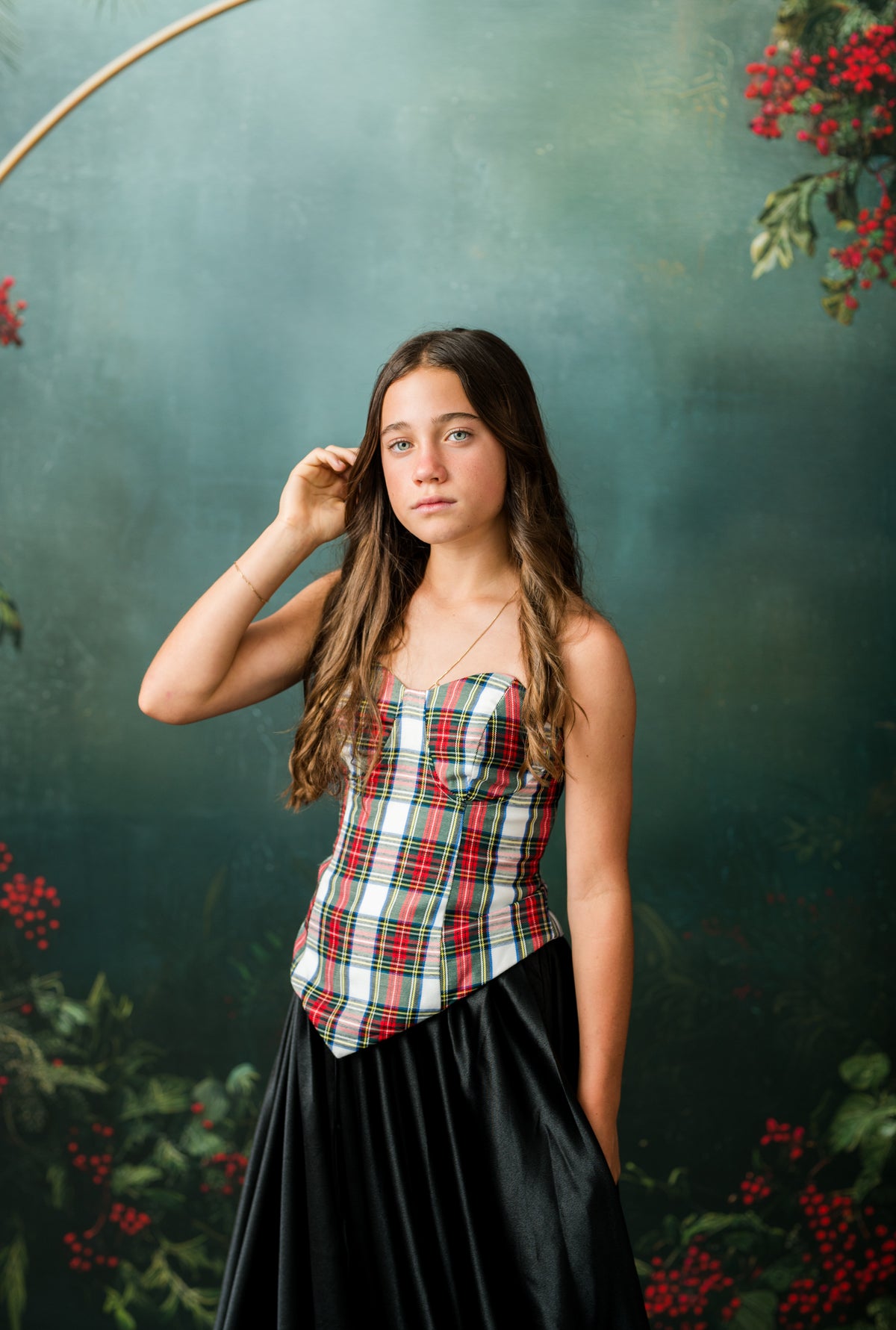 Teen model in dramatic red satin Christmas gown against an evergreen holiday backdrop