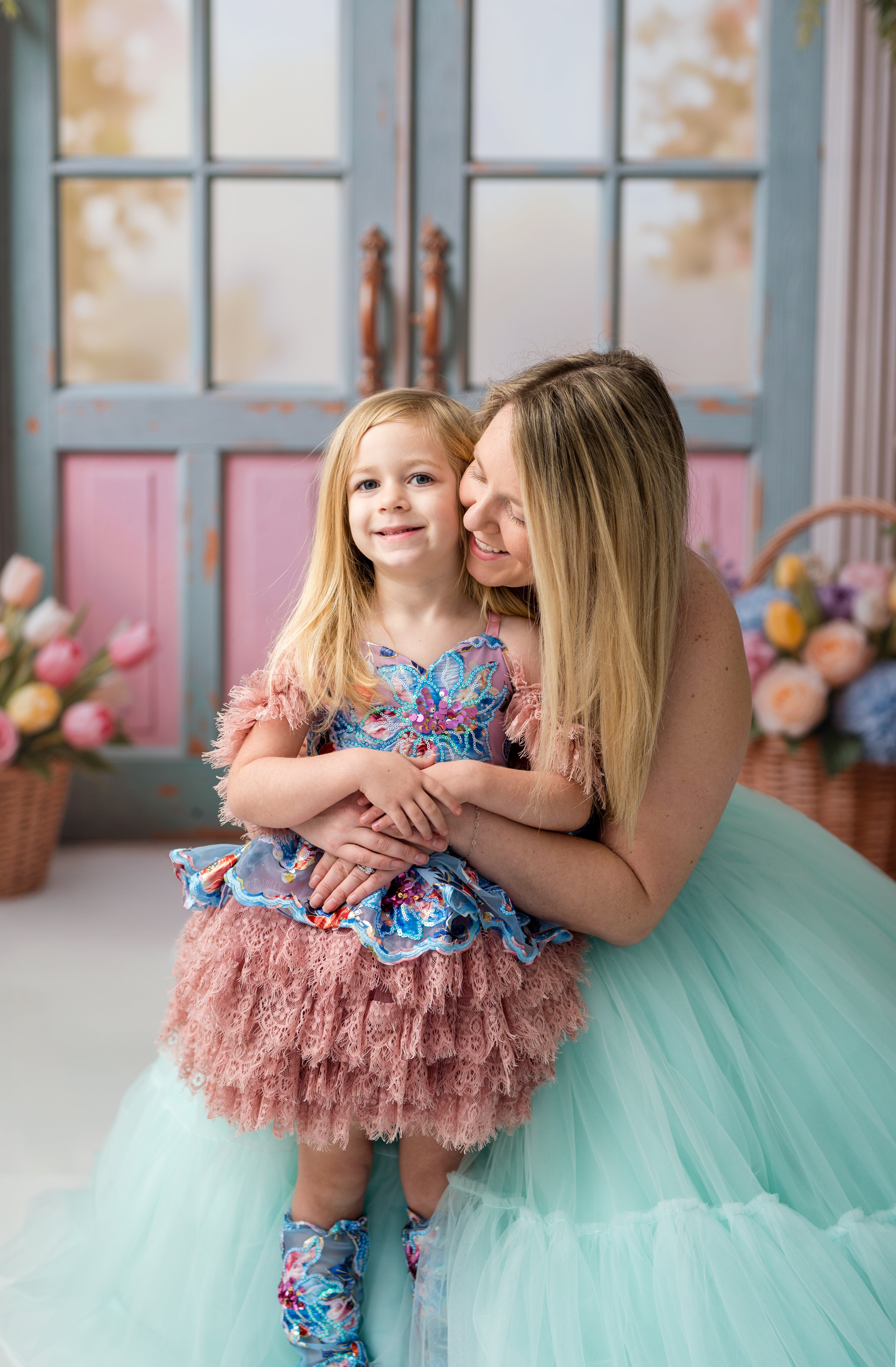 Woman and child in formal dresses standing close together with a floral arrangement in the background.