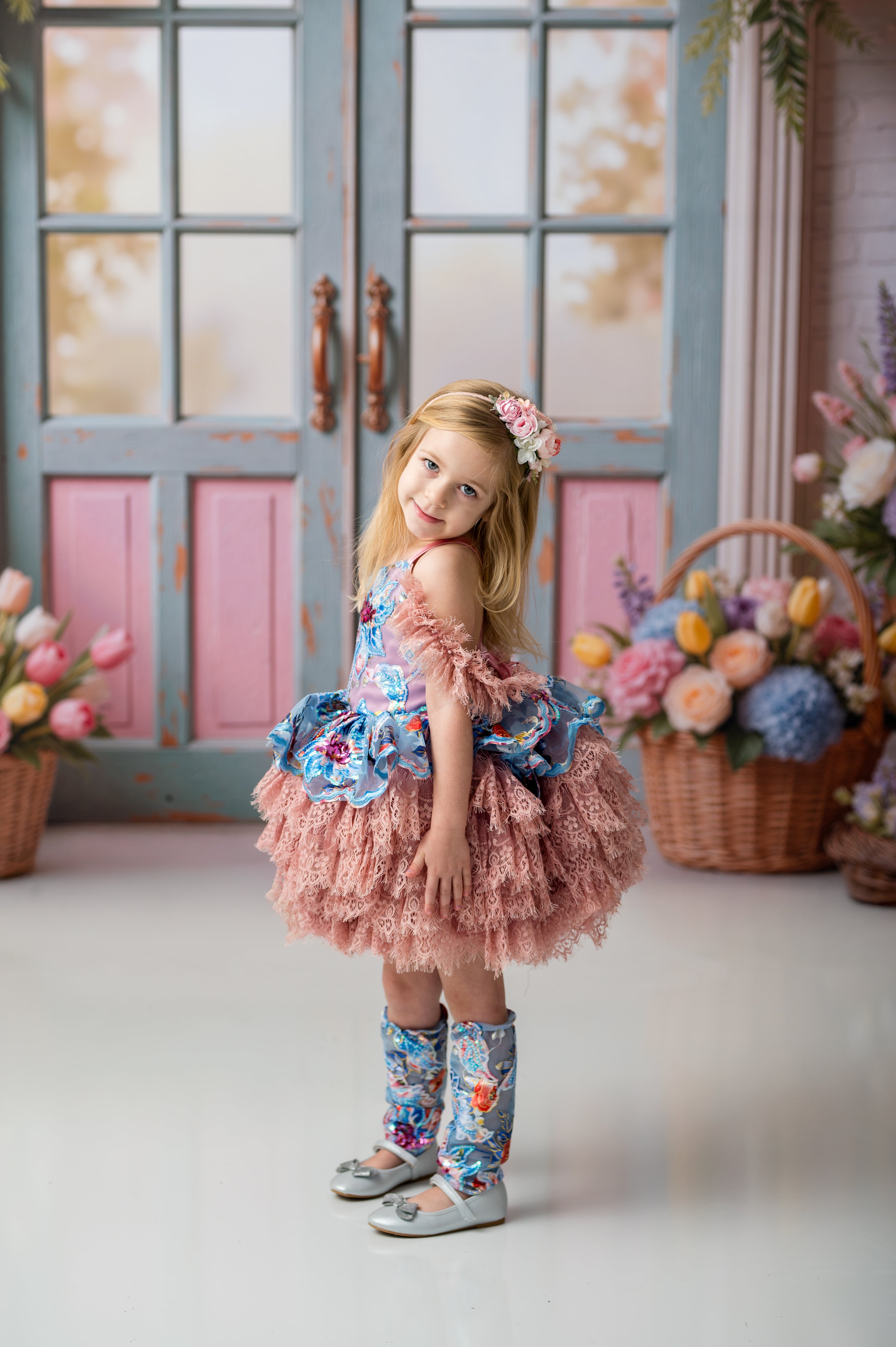 Young girl in a floral dress standing in a decorated room with flowers and a pink door.