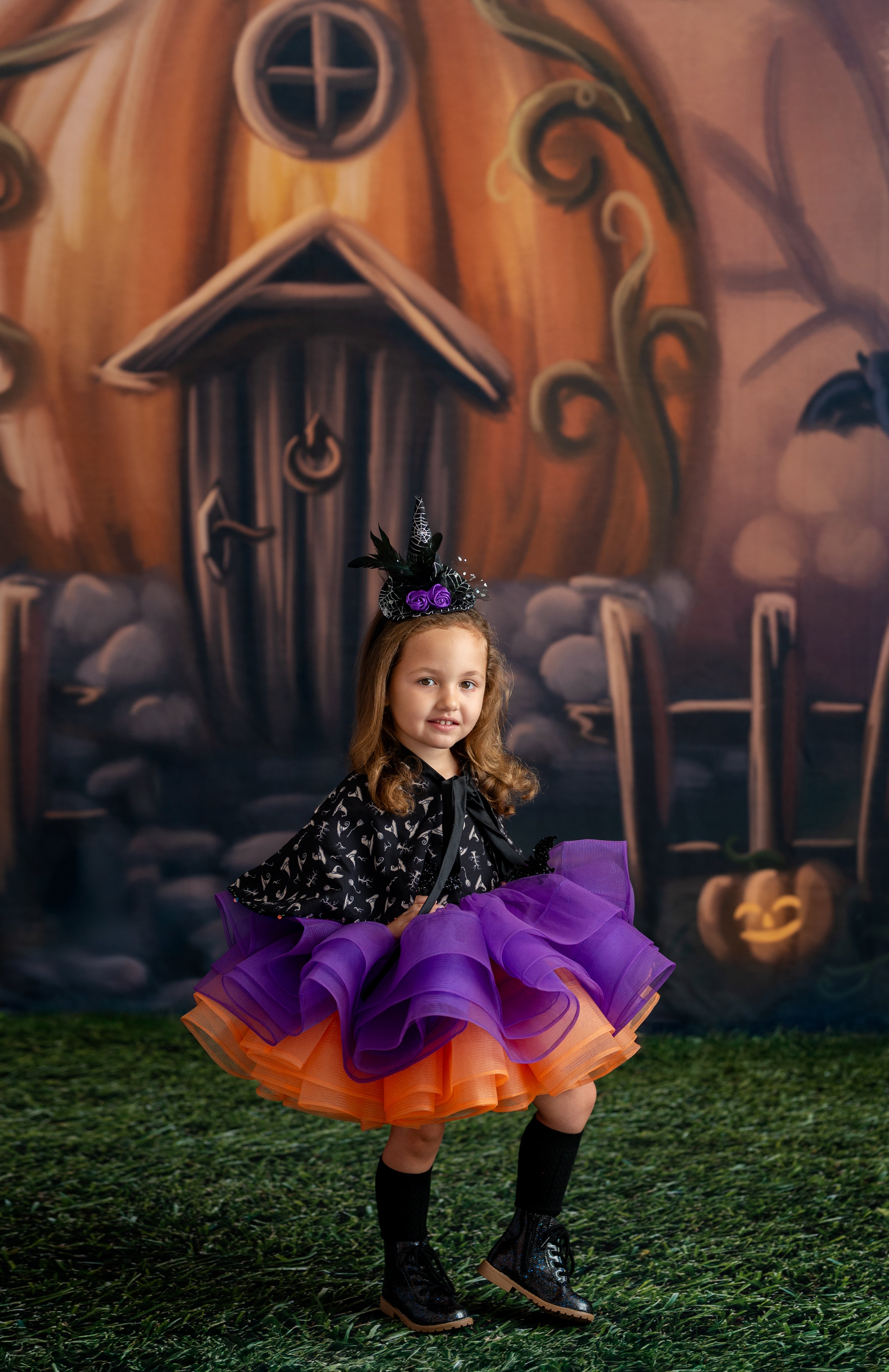 Young girl in a Halloween costume standing in front of a pumpkin house backdrop