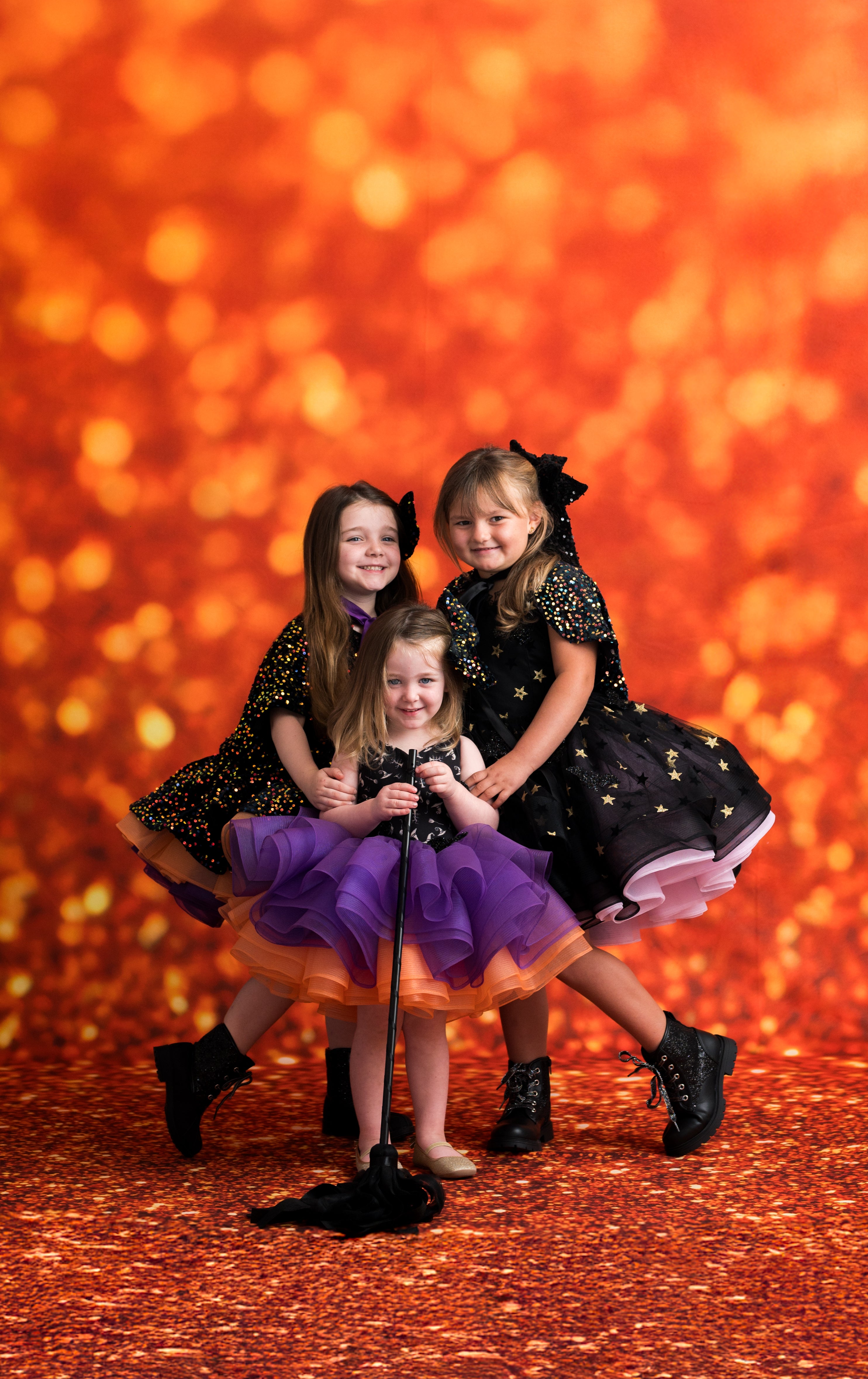 Three children in black and purple dresses posing against a warm orange background
