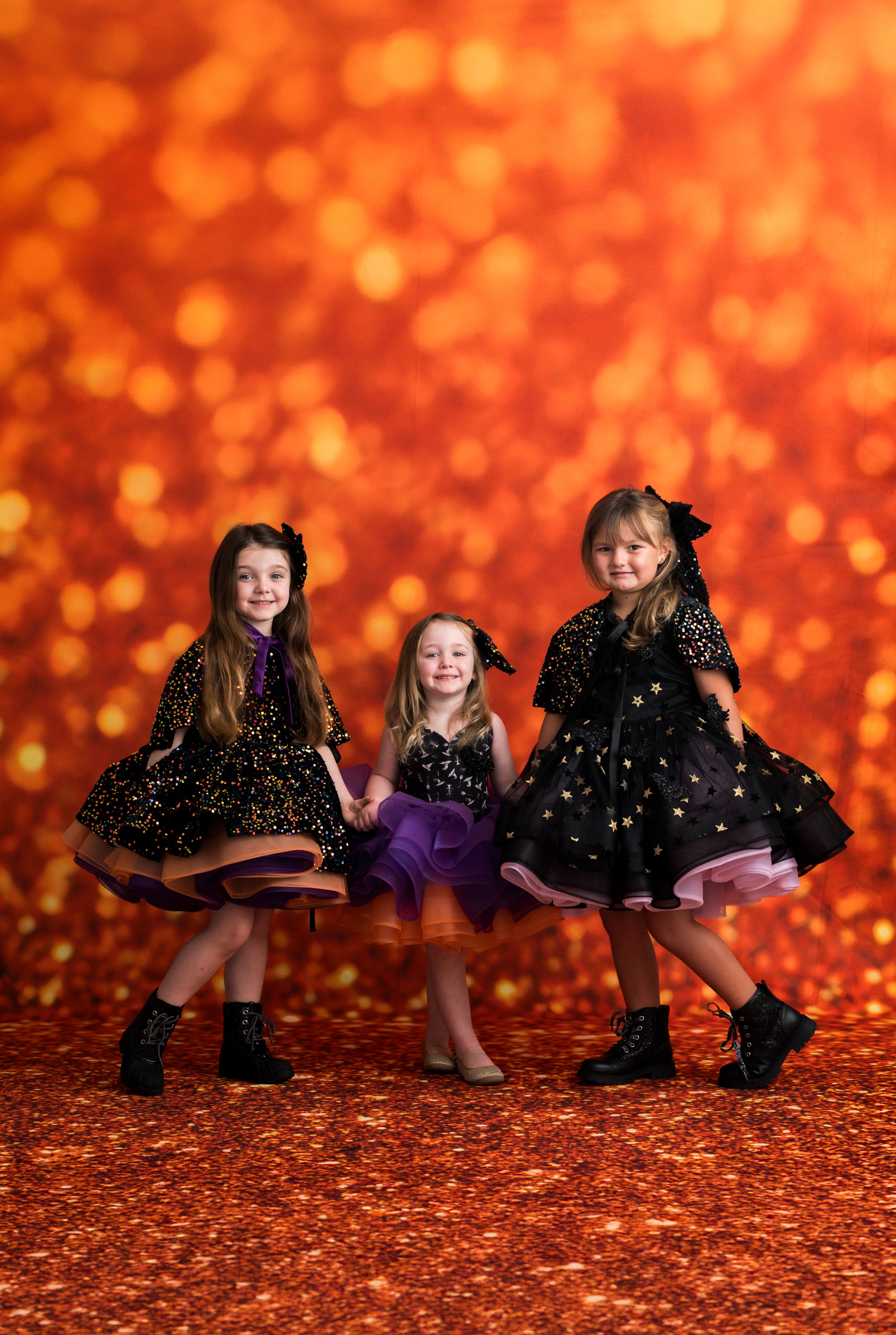 Three young girls in black dresses with star patterns against a warm, glowing background.
