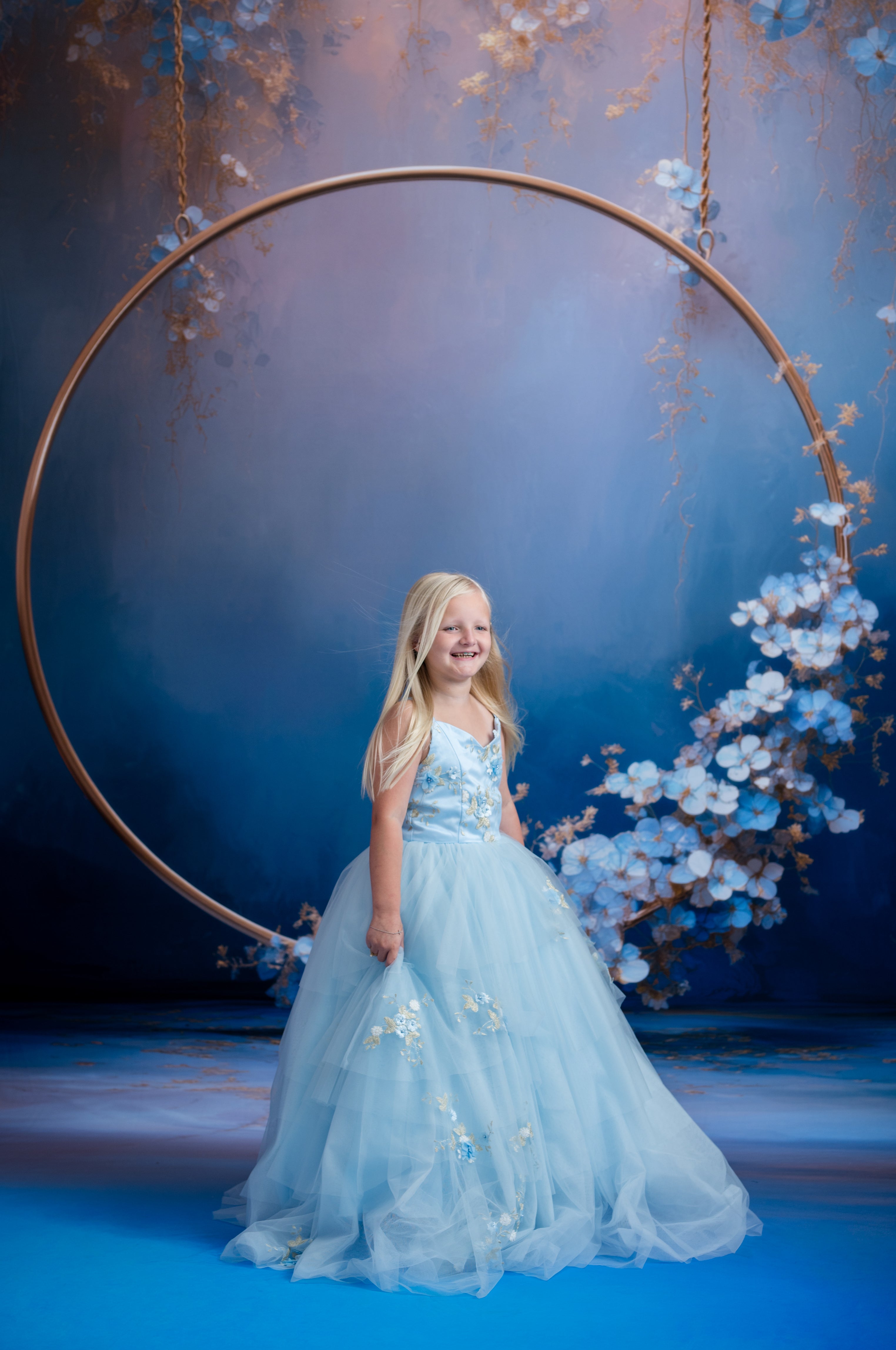 Young girl in a blue dress standing under a floral arch with a blue background