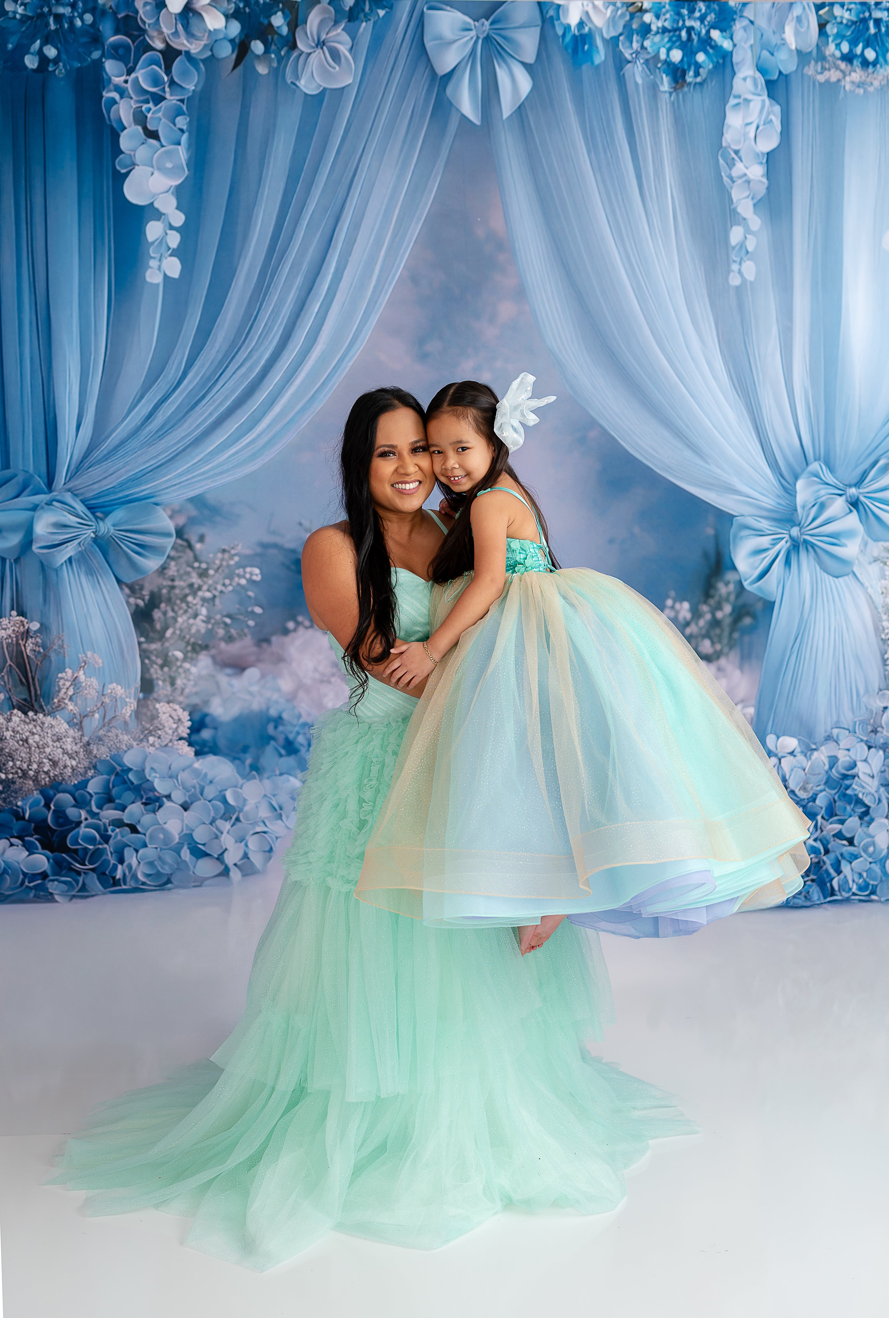 "Elegant mommy and me moment with a mother and daughter in flowing pastel blue-green dresses."