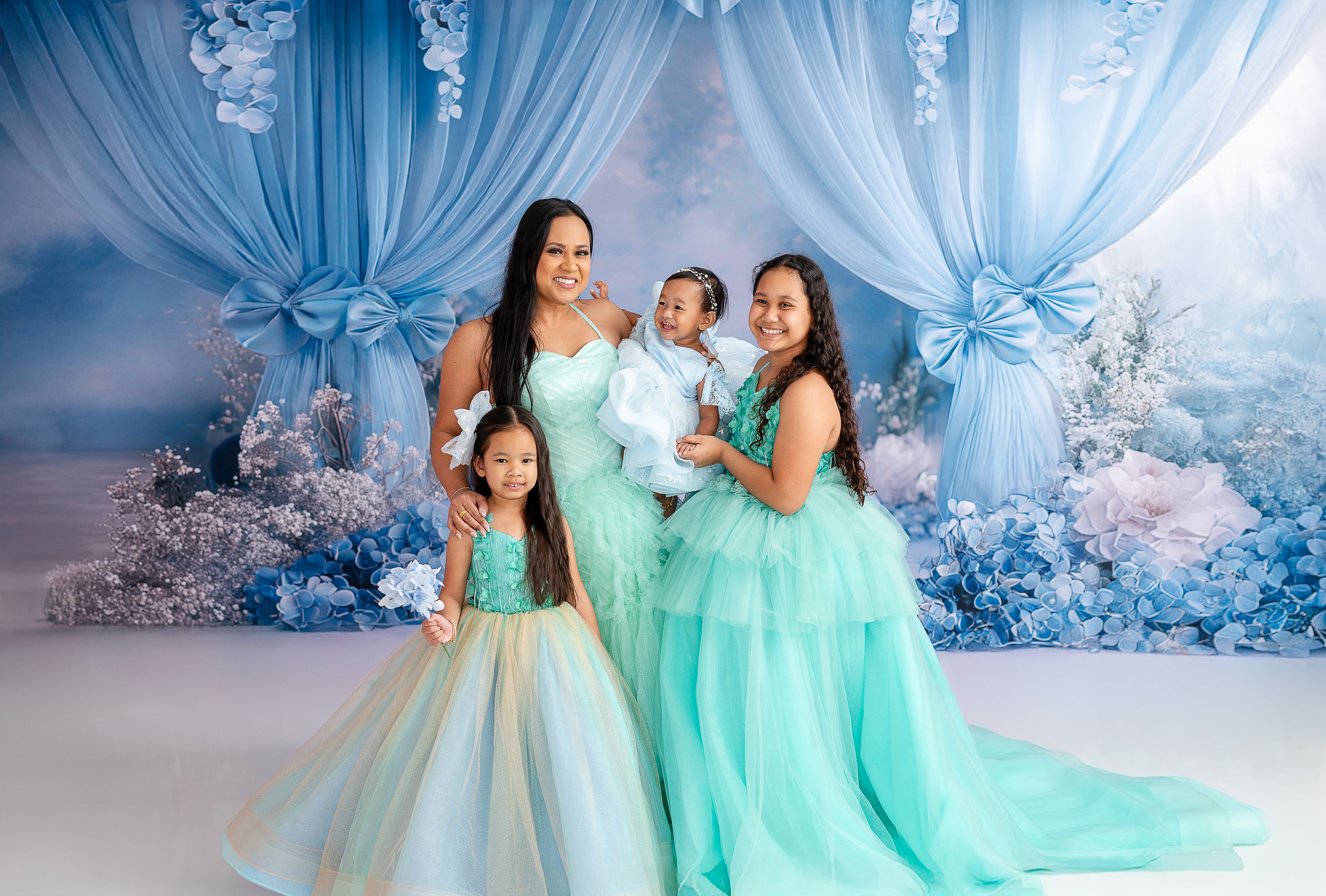"Whimsical mommy and me portrait featuring elegant tulle gowns and a floral blue backdrop."