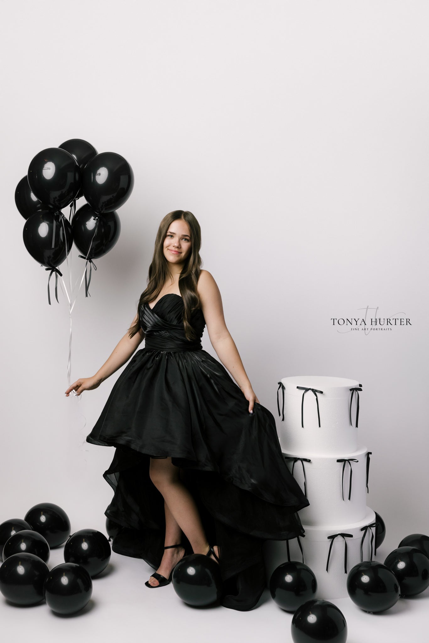 Woman in a black dress holding black balloons against a white background