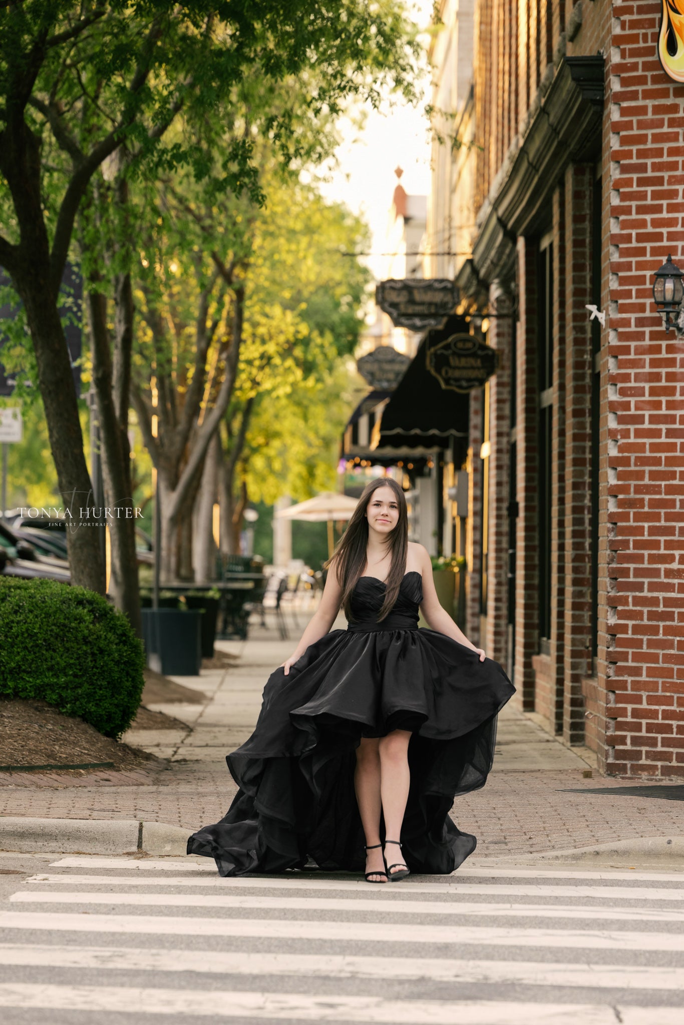 Woman in a black dress standing on a city street with trees and buildings in the background
