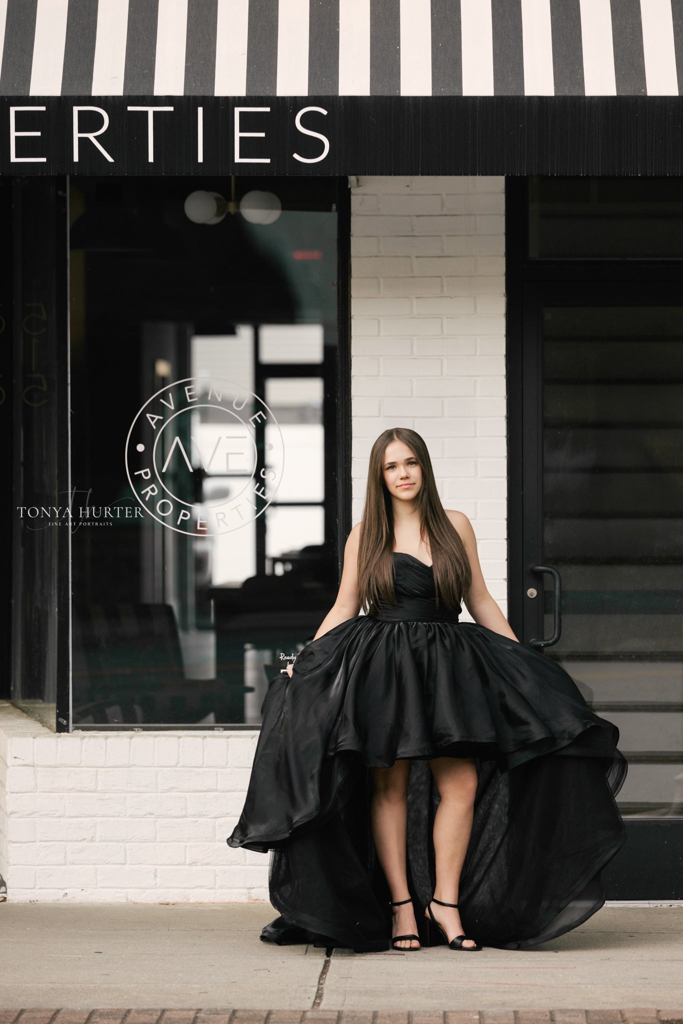 Woman in a black dress standing in front of a building with 'Avenue Properties' branding.