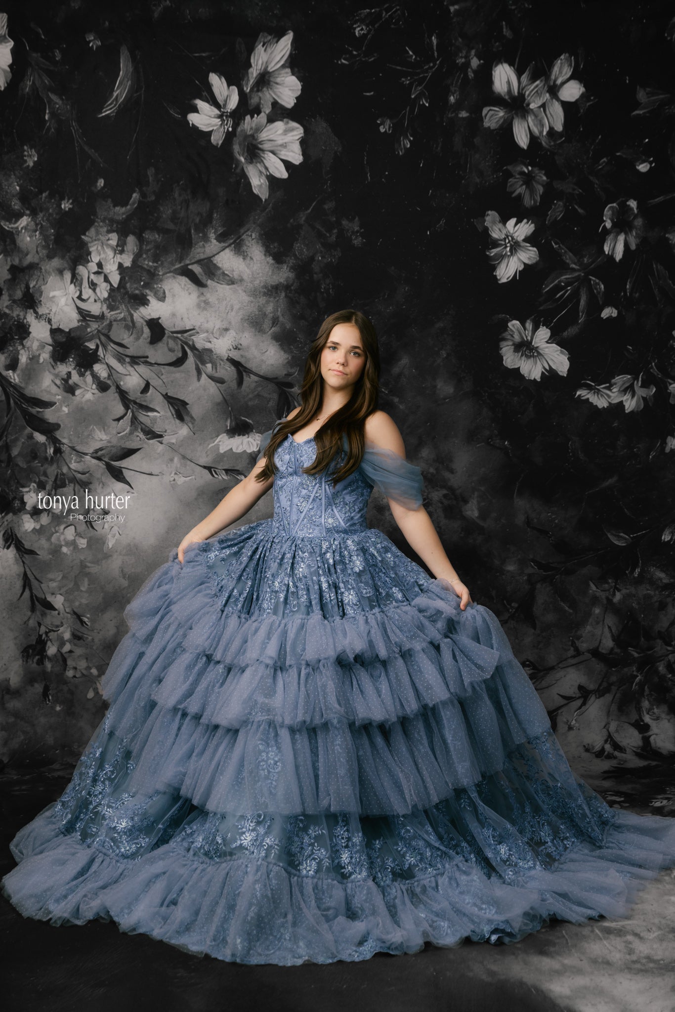 Woman in a blue gown against a dark floral backdrop