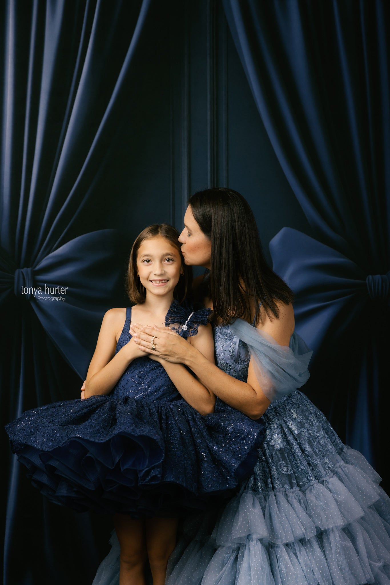 Two women in formal dresses posing against a dark curtain