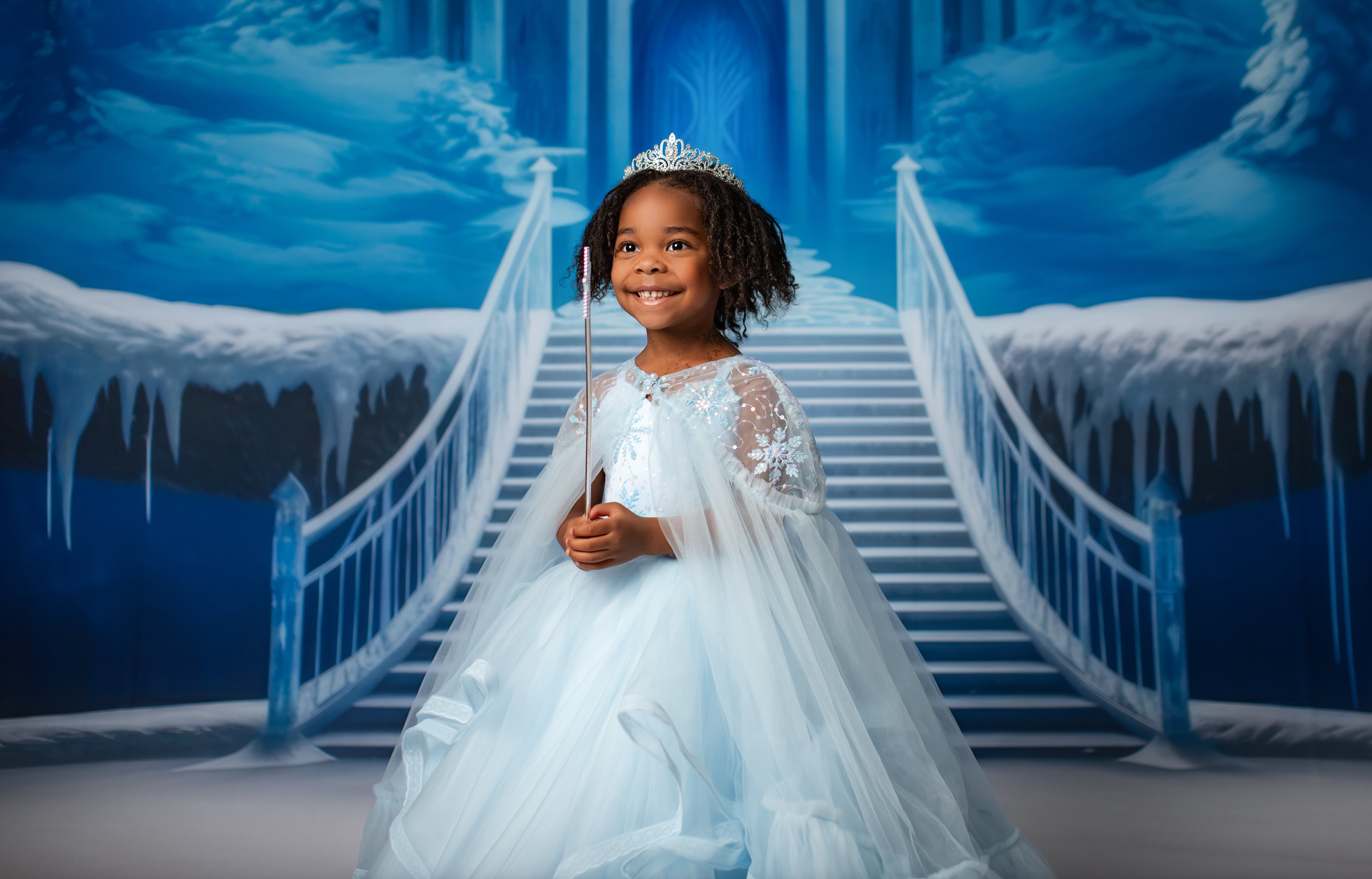 Elegant, Elsa-inspired gown in a frosty blue with sparkling accents, worn by a model in a snowy photoshoot setting. Perfect for winter and holiday photography.