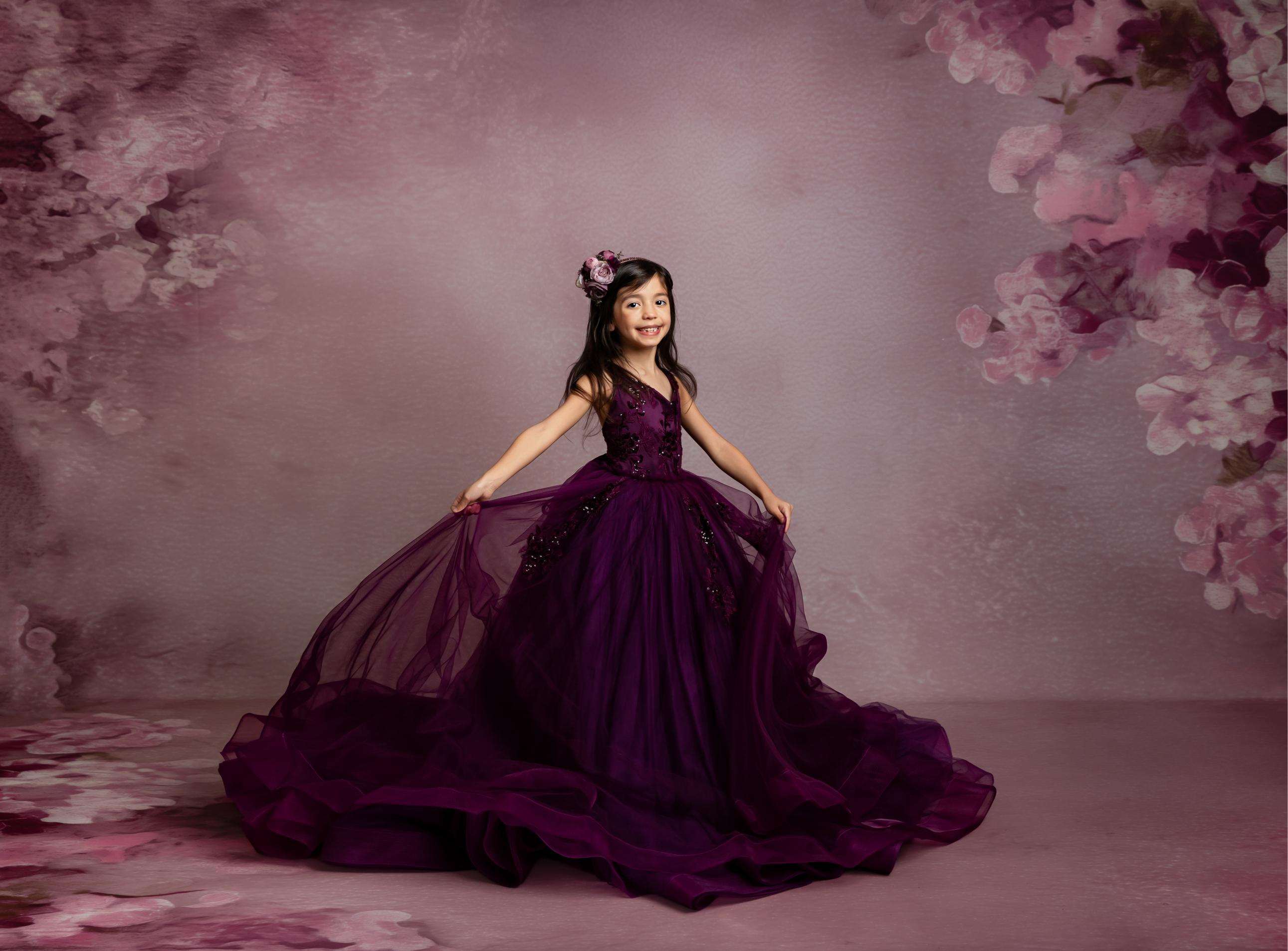 Young girl in a purple gown standing against a floral backdrop