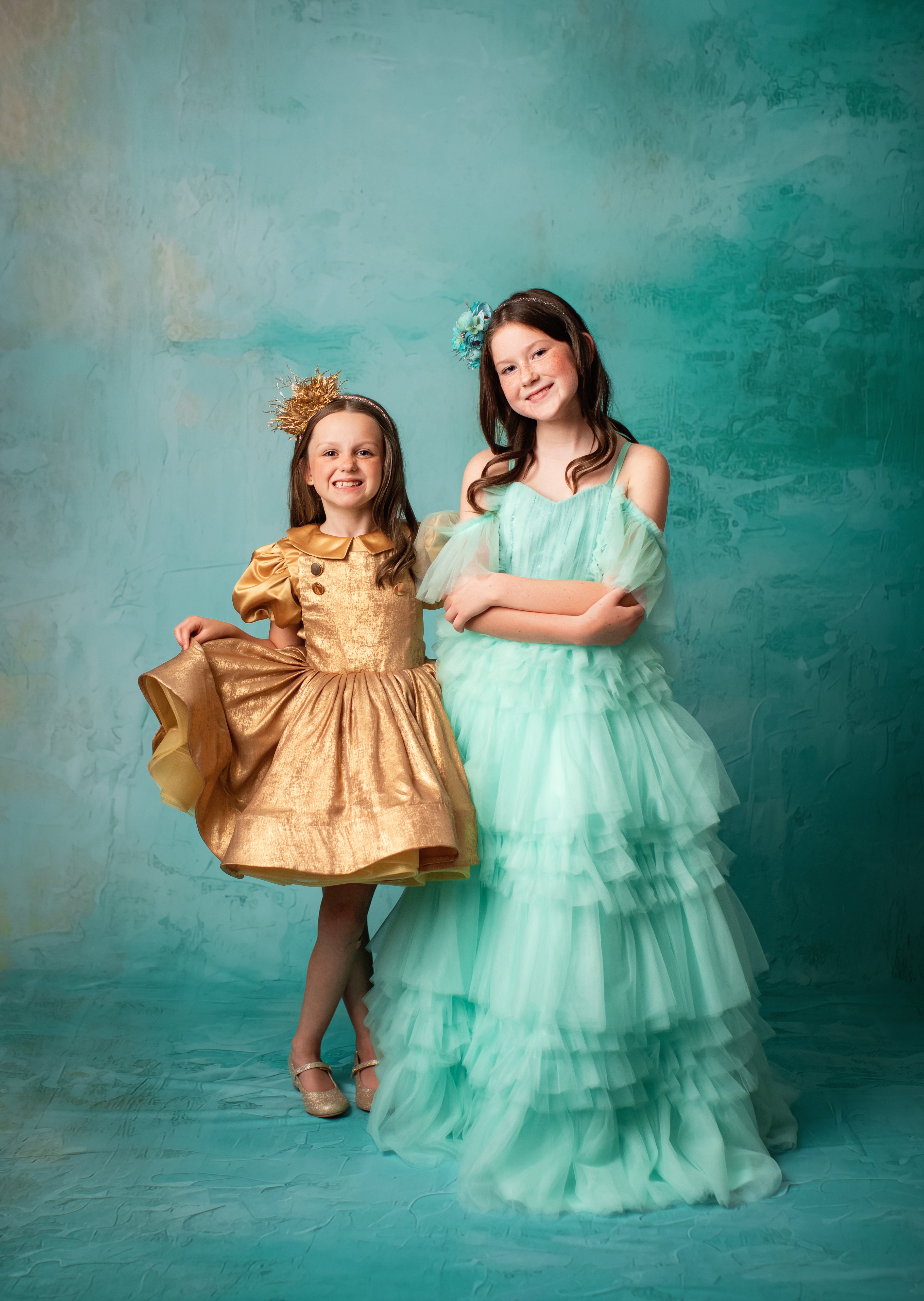 "Girl in a flowing mint green gown standing against a teal backdrop."