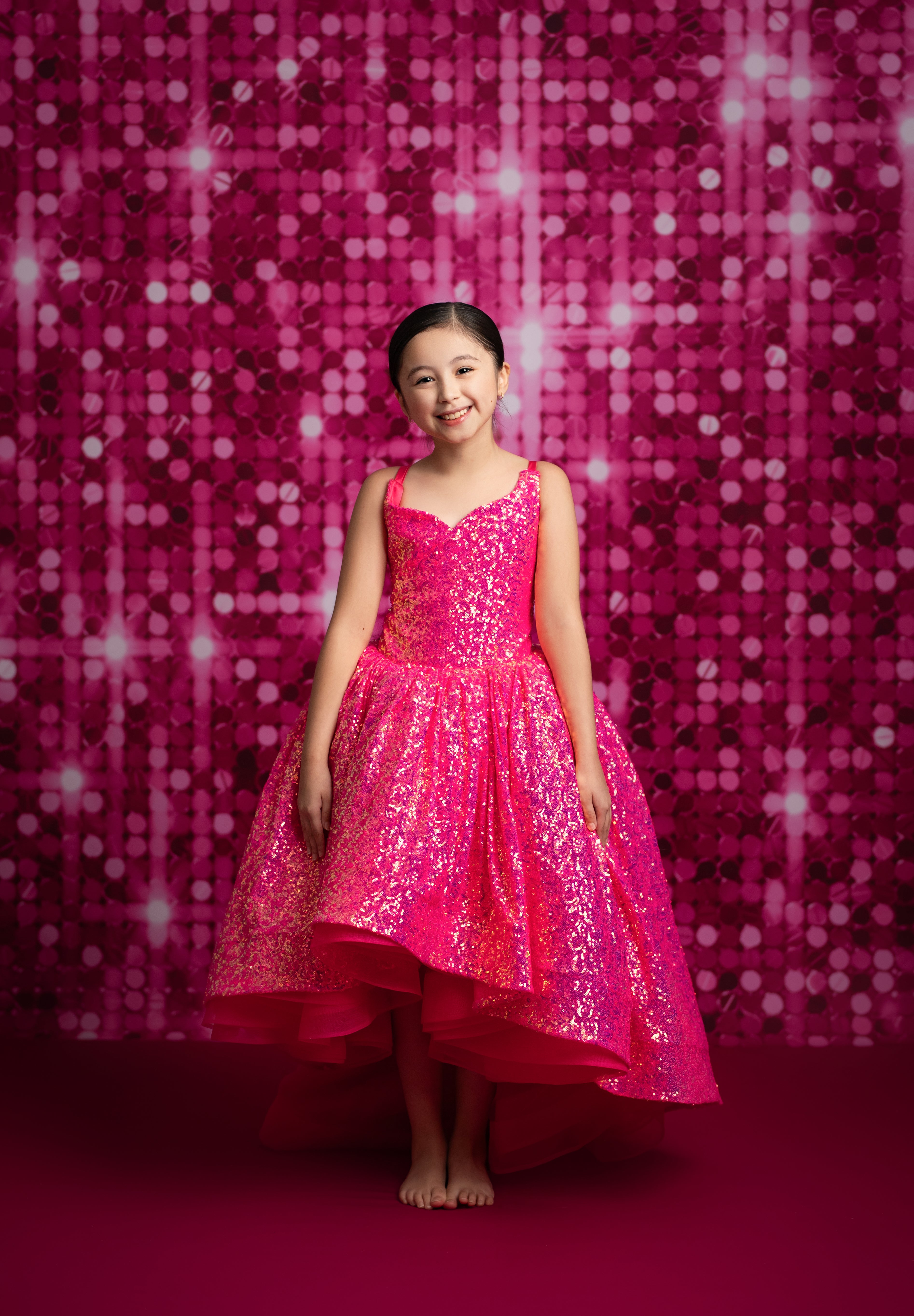 Young girl in a pink dress standing against a pink sequin backdrop