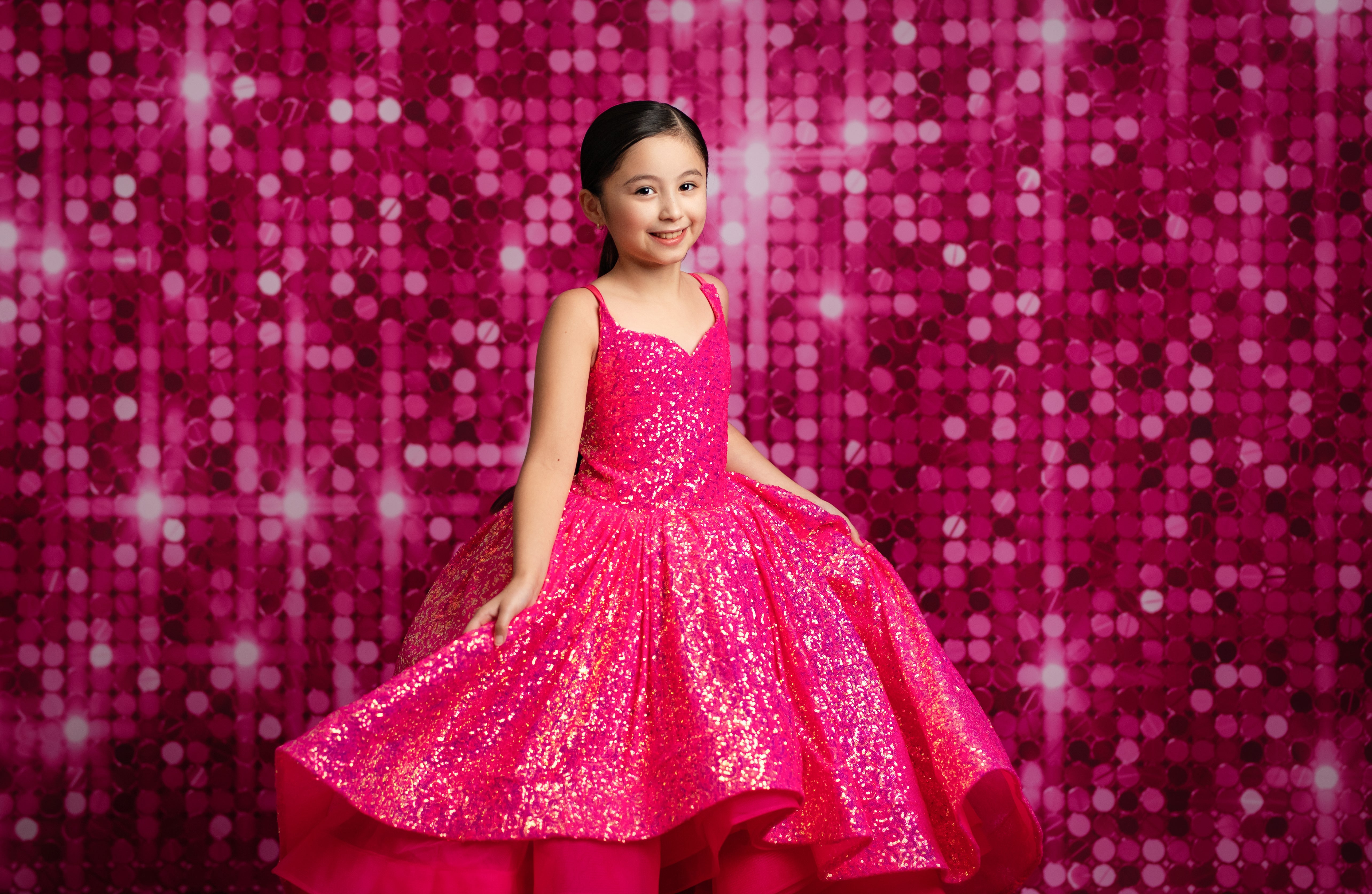 Young girl in a pink sequined dress against a pink glittery background