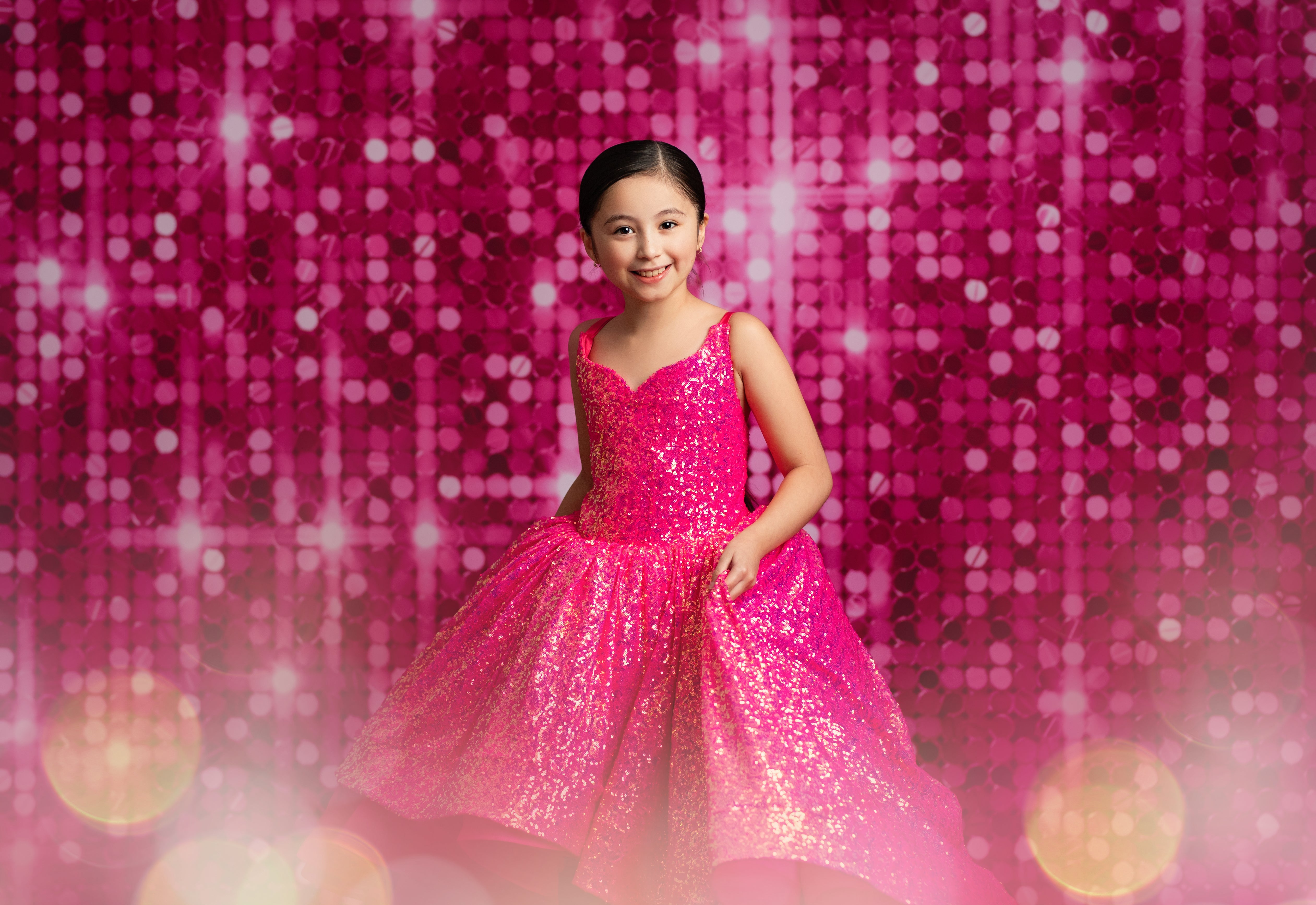 Young girl in a pink sequin dress against a pink glittery background
