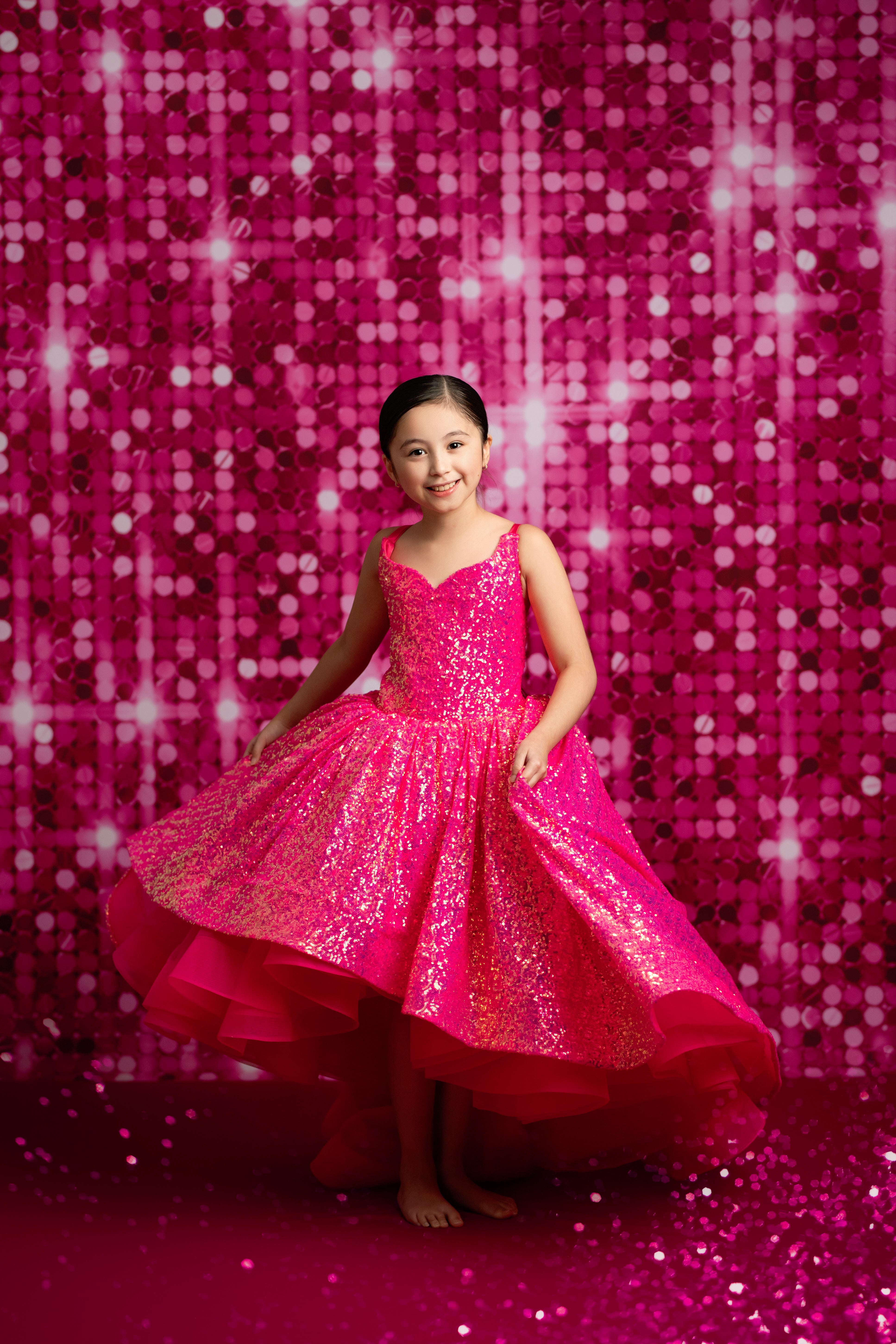 Young girl in a pink sparkly dress standing against a pink sequin backdrop