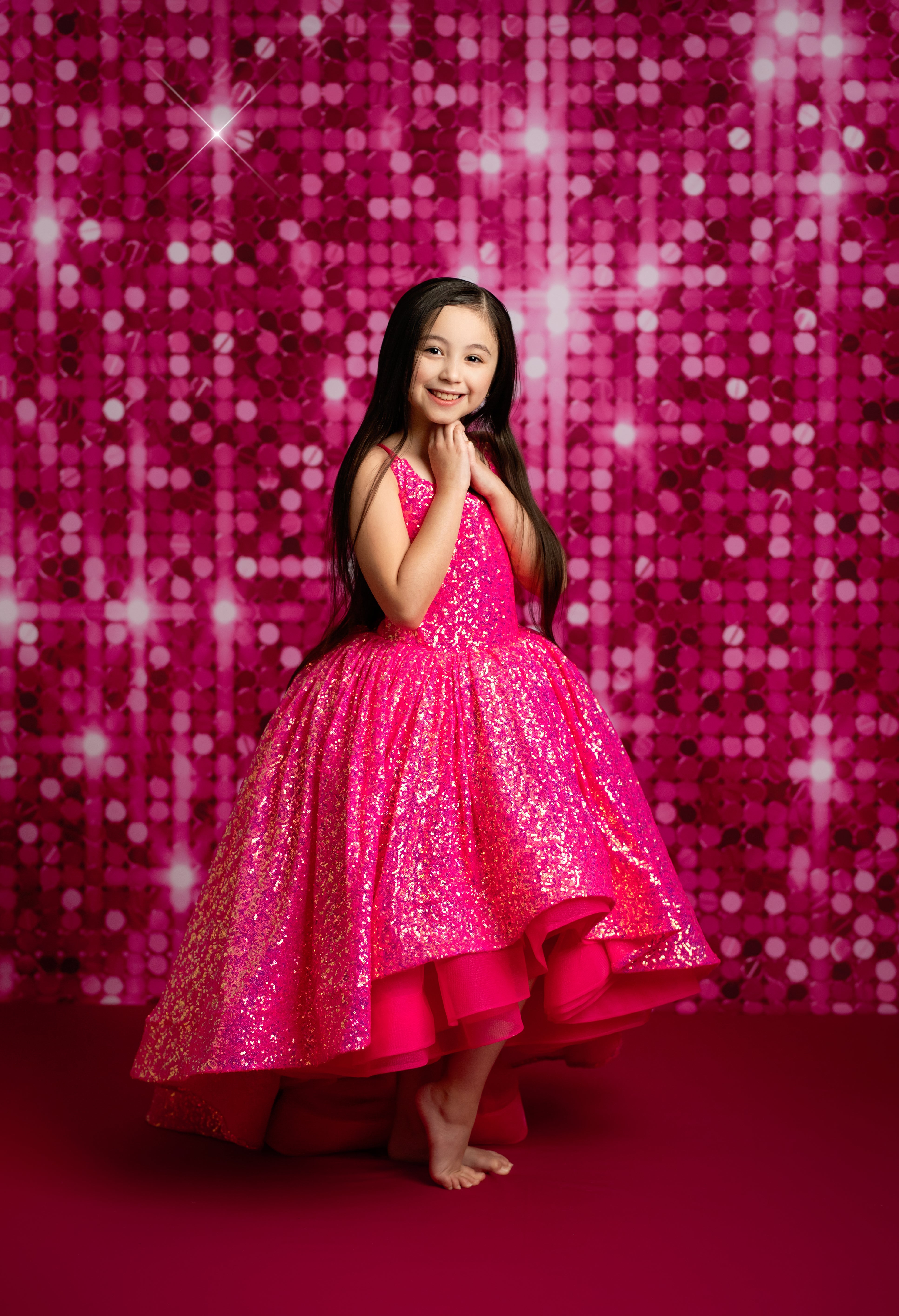 Young girl in a pink sparkly dress posing against a pink sequin backdrop