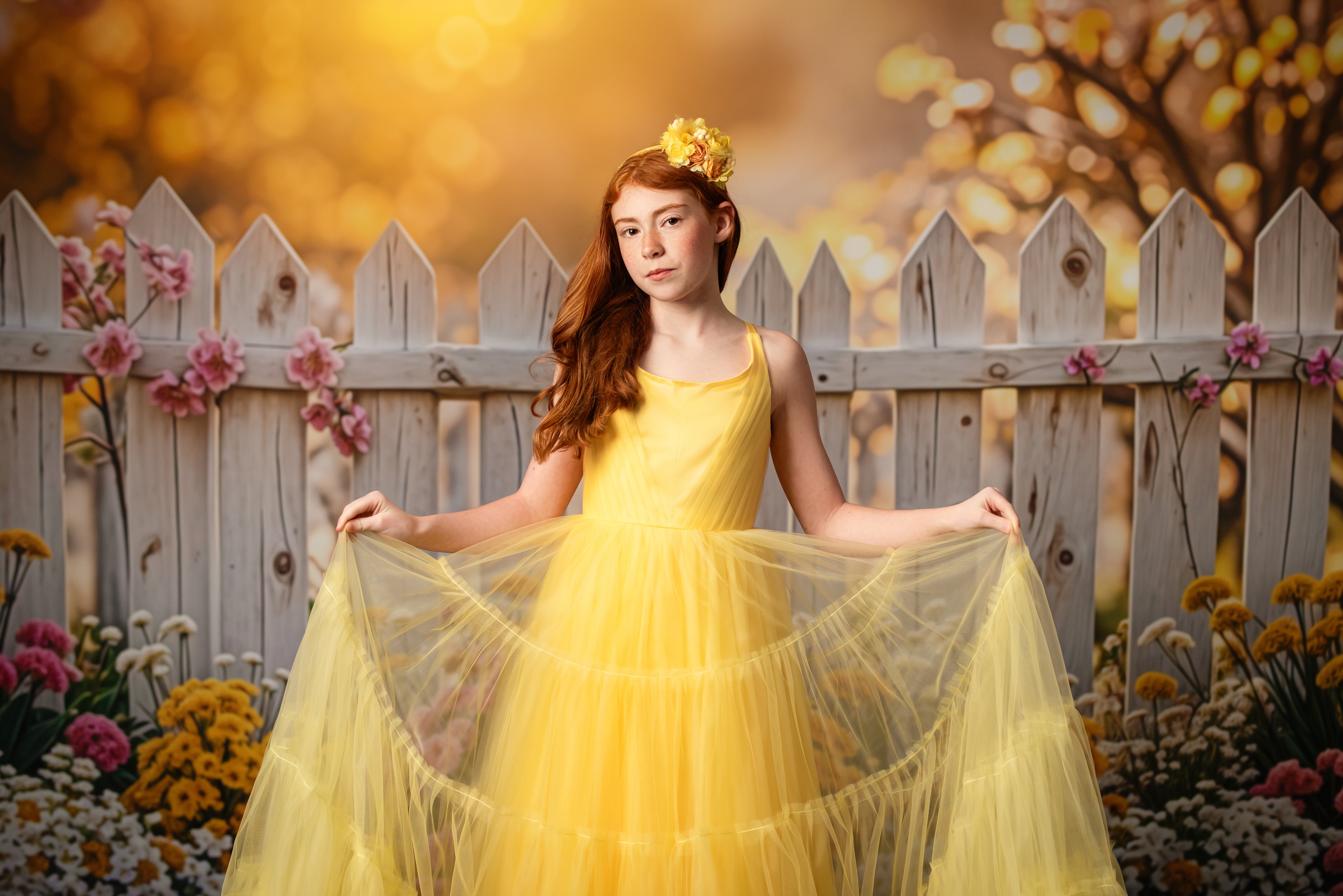 Sunshine elegance – A red-haired girl in a vibrant yellow dress holds out her gown, surrounded by a dreamy autumn-inspired backdrop.
