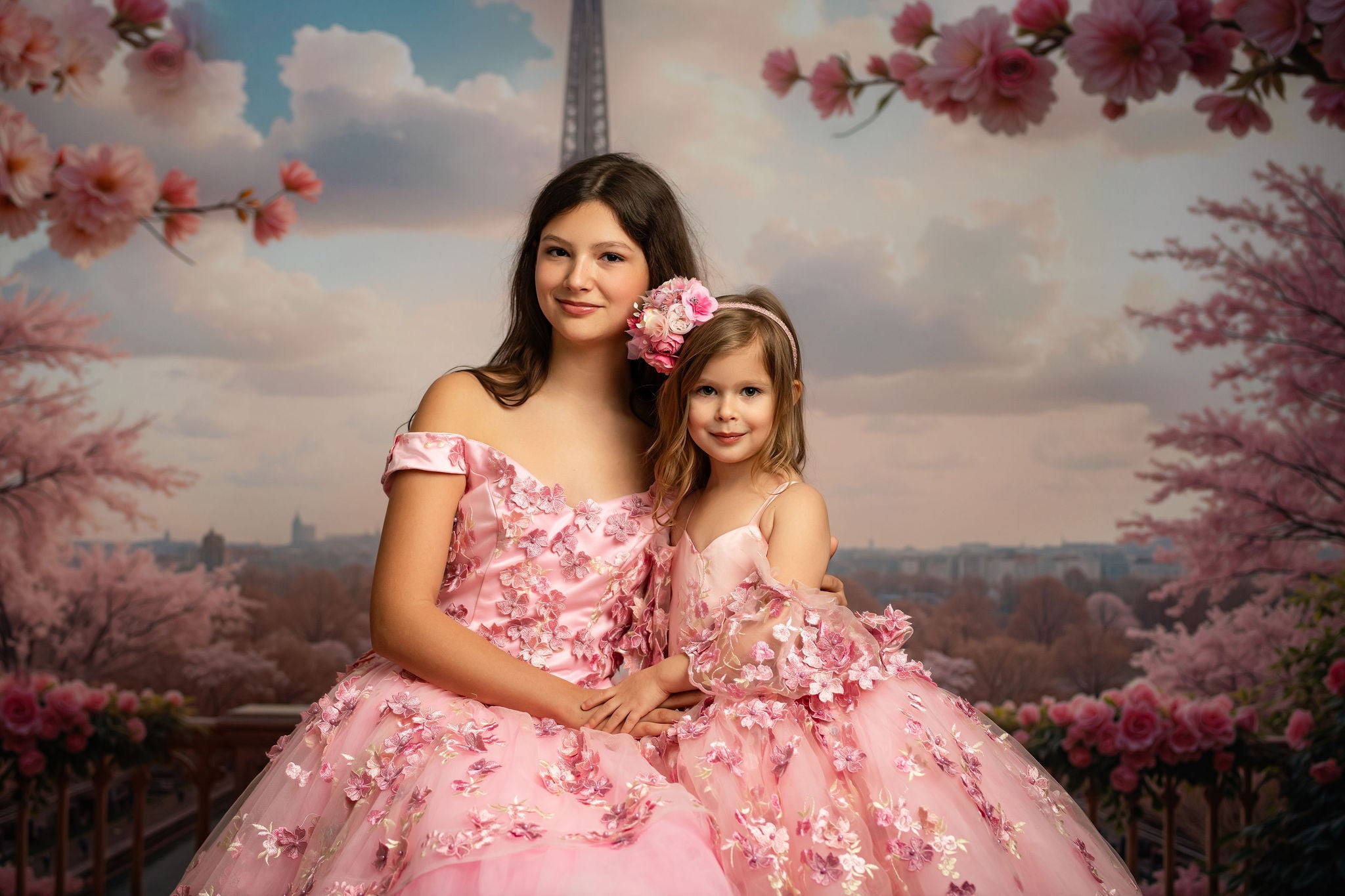 Two women in pink floral dresses sitting together with cherry blossom trees and the Eiffel Tower in the background.