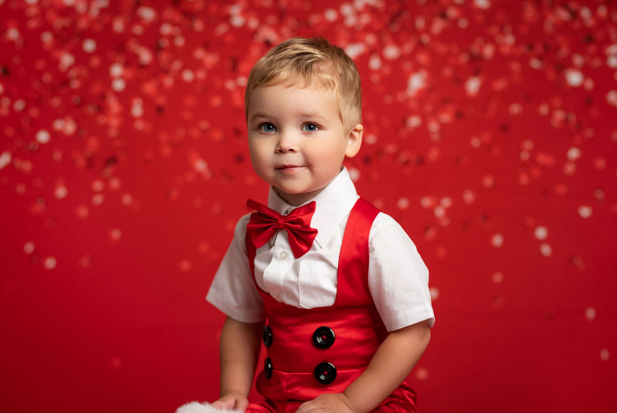 Child in a red outfit with suspenders and bow tie against a red background
