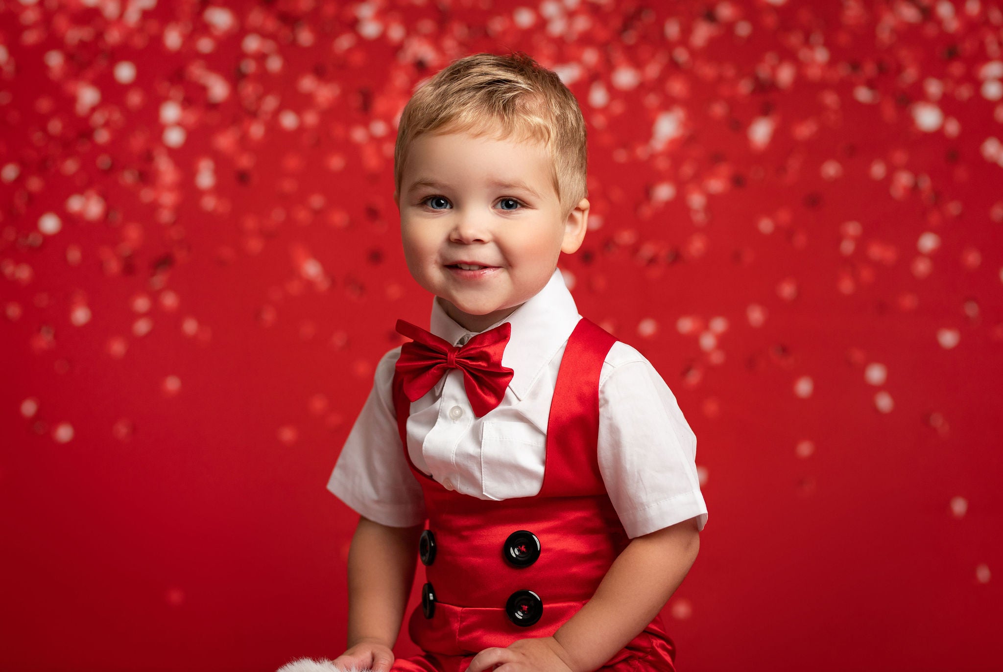 Child wearing a red outfit with suspenders and a bow tie against a red background