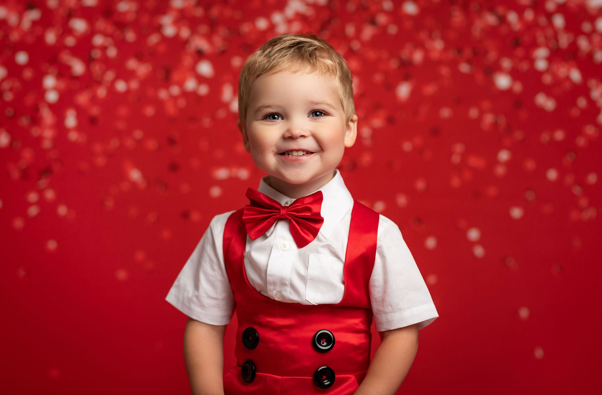 Child wearing a red vest and bow tie against a red background with white polka dots