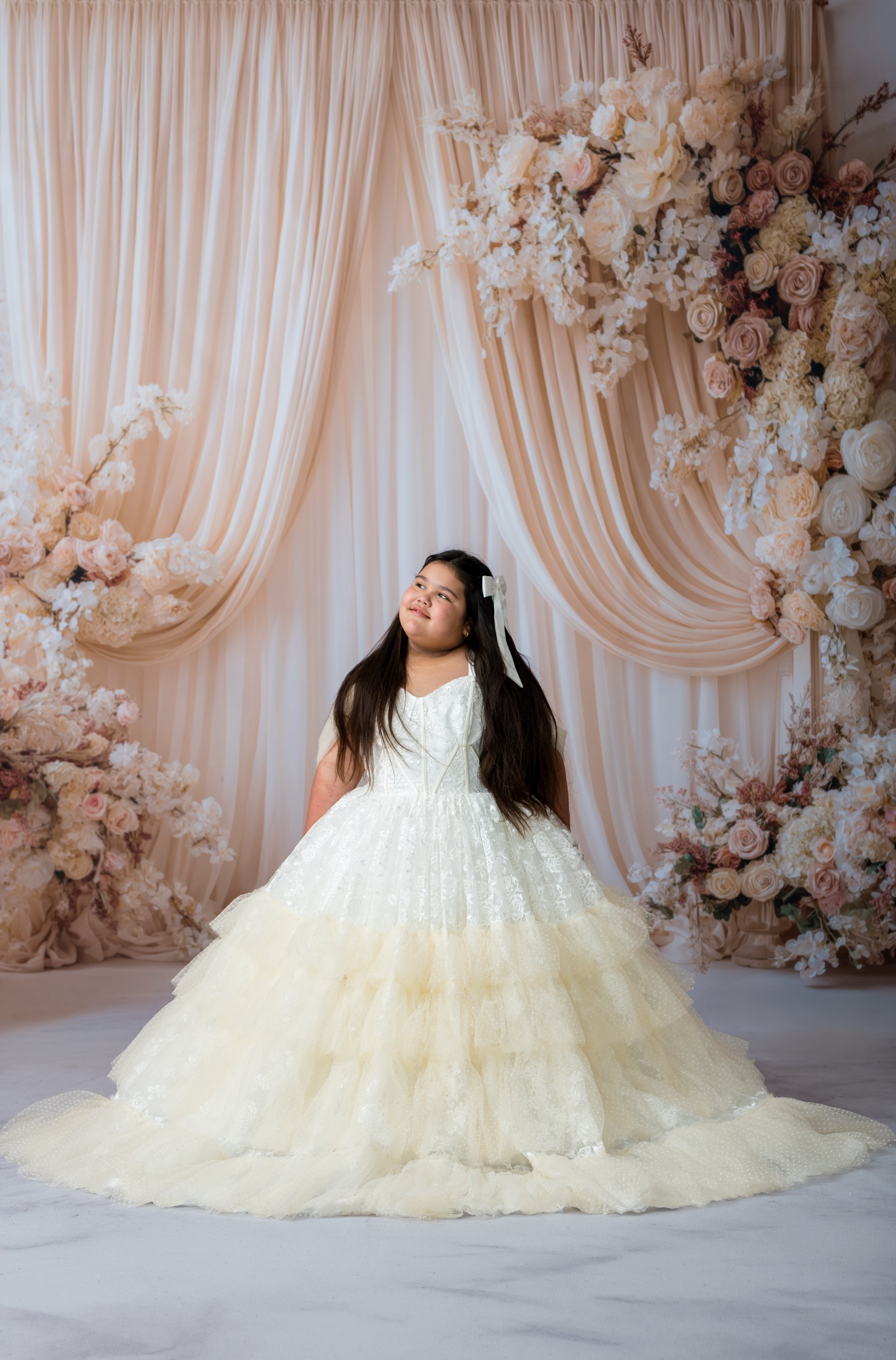 Woman in a white wedding dress standing in front of a floral arch and draped curtains.