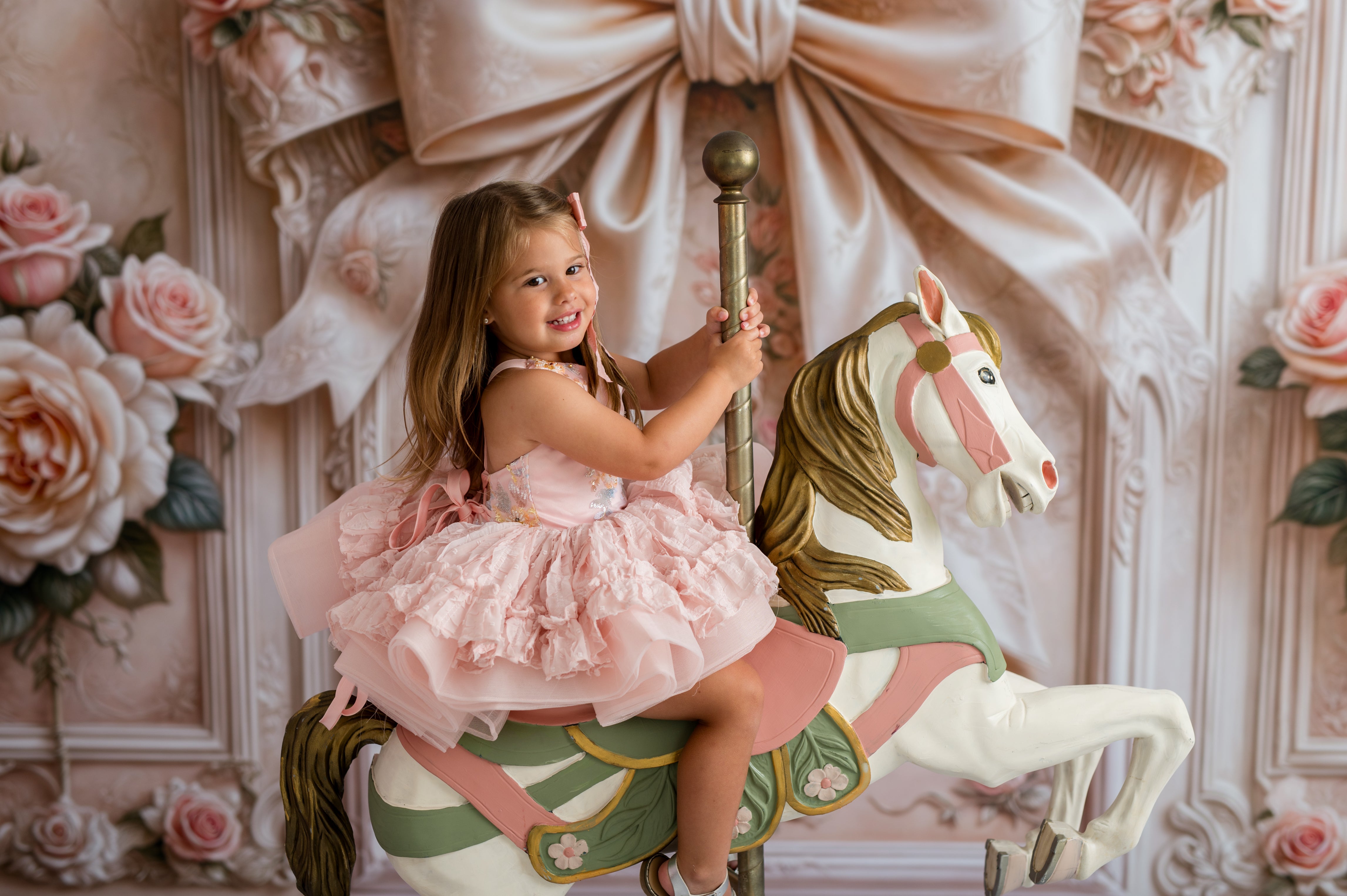 Young girl in a pink dress riding a carousel horse with floral and decorative wall background