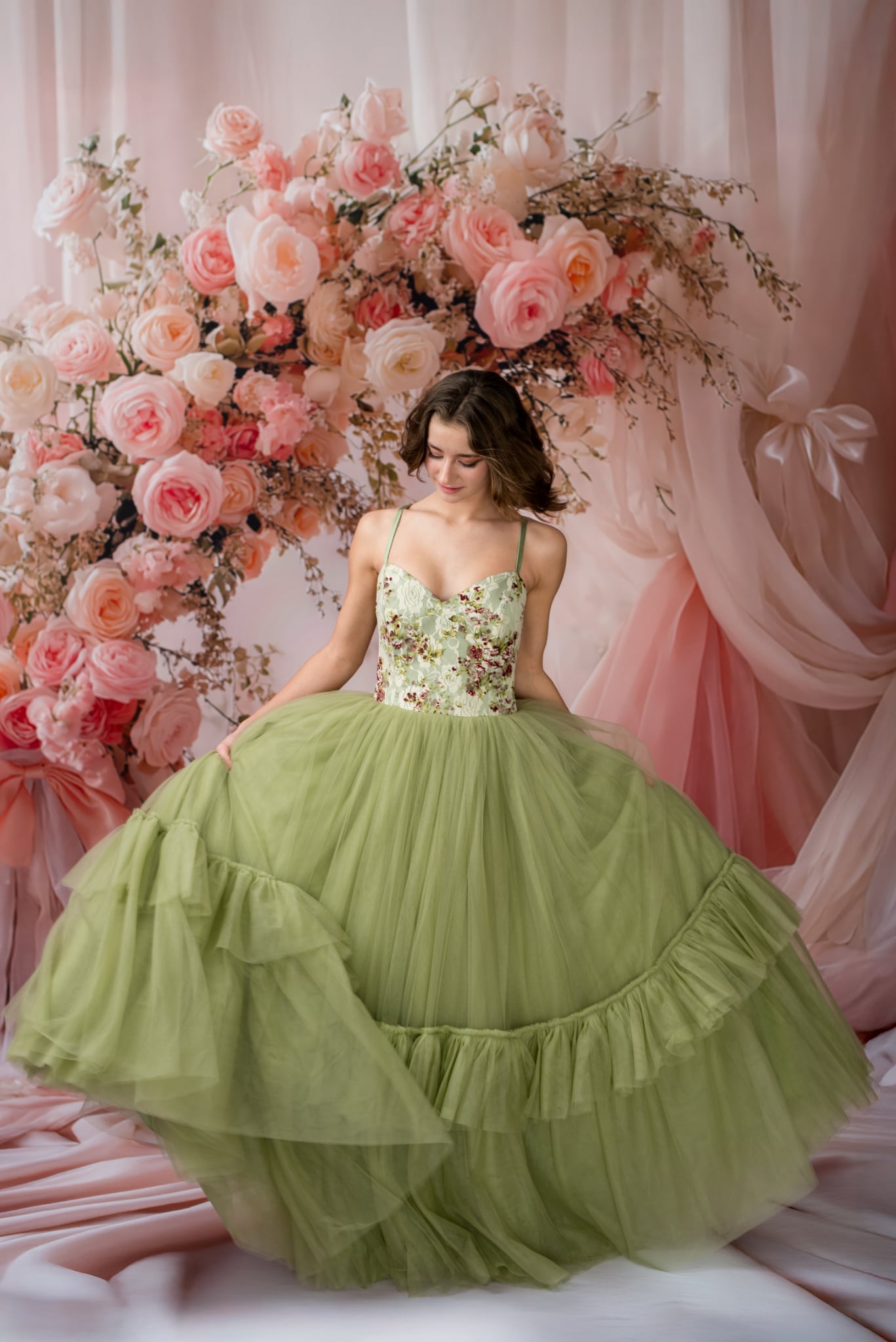 Woman in a green floral dress standing in front of a floral arch with pink and white flowers.